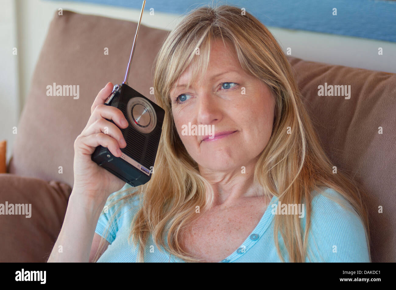 Donna bionda con espressione piacevole holding radio a transistor al suo orecchio. Foto Stock