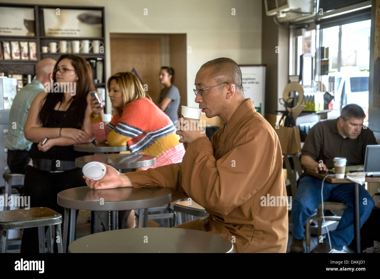 In contrasto con i dintorni, un asiatico monaco buddista in marrone accappatoi e testa rasata, aggiorna se stesso a uno Starbucks Cafe. Foto Stock