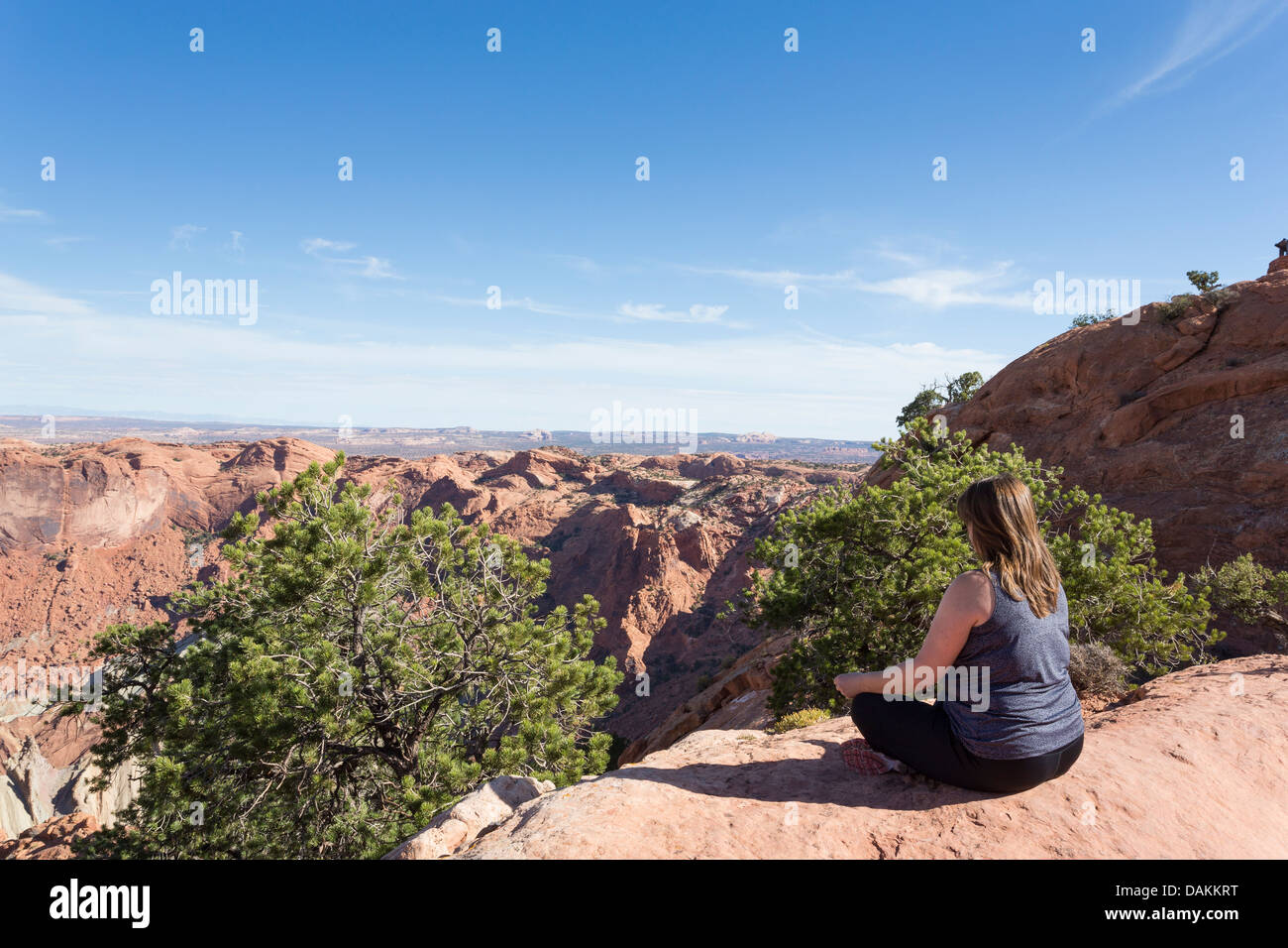 Donna rilassarsi sul bordo del canyon lungo il sentiero nel Parco Nazionale di Canyonlands, Utah Foto Stock