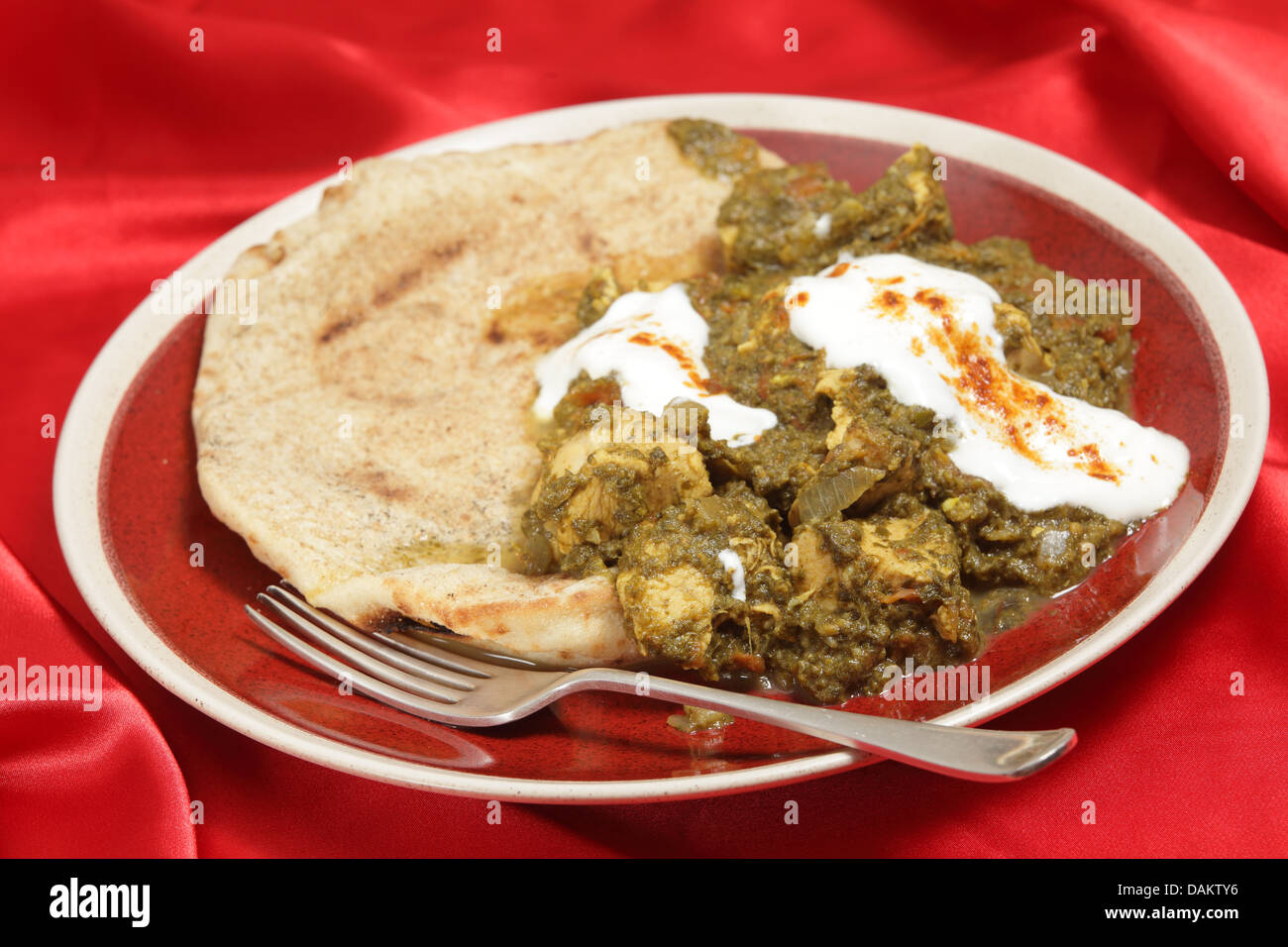 Saag pollo al curry, servita con pane piatto e yogurt cosparso con peperoncino rosso. Foto Stock