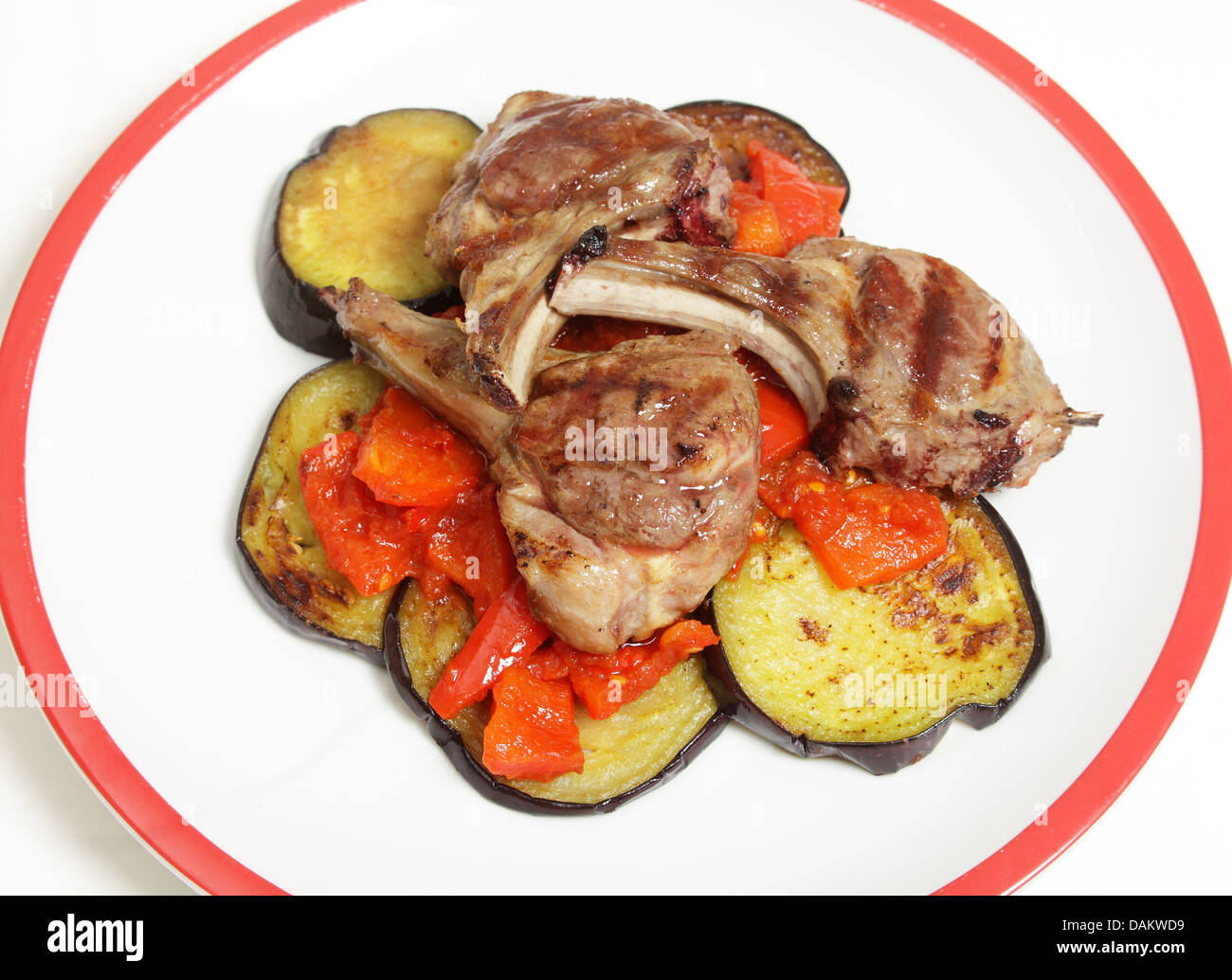 Tre costolette di agnello grigliate su un letto di oliva-oul melanzane fritte e le fette di pomodoro, peperoncino e salsa di peperoni Foto Stock