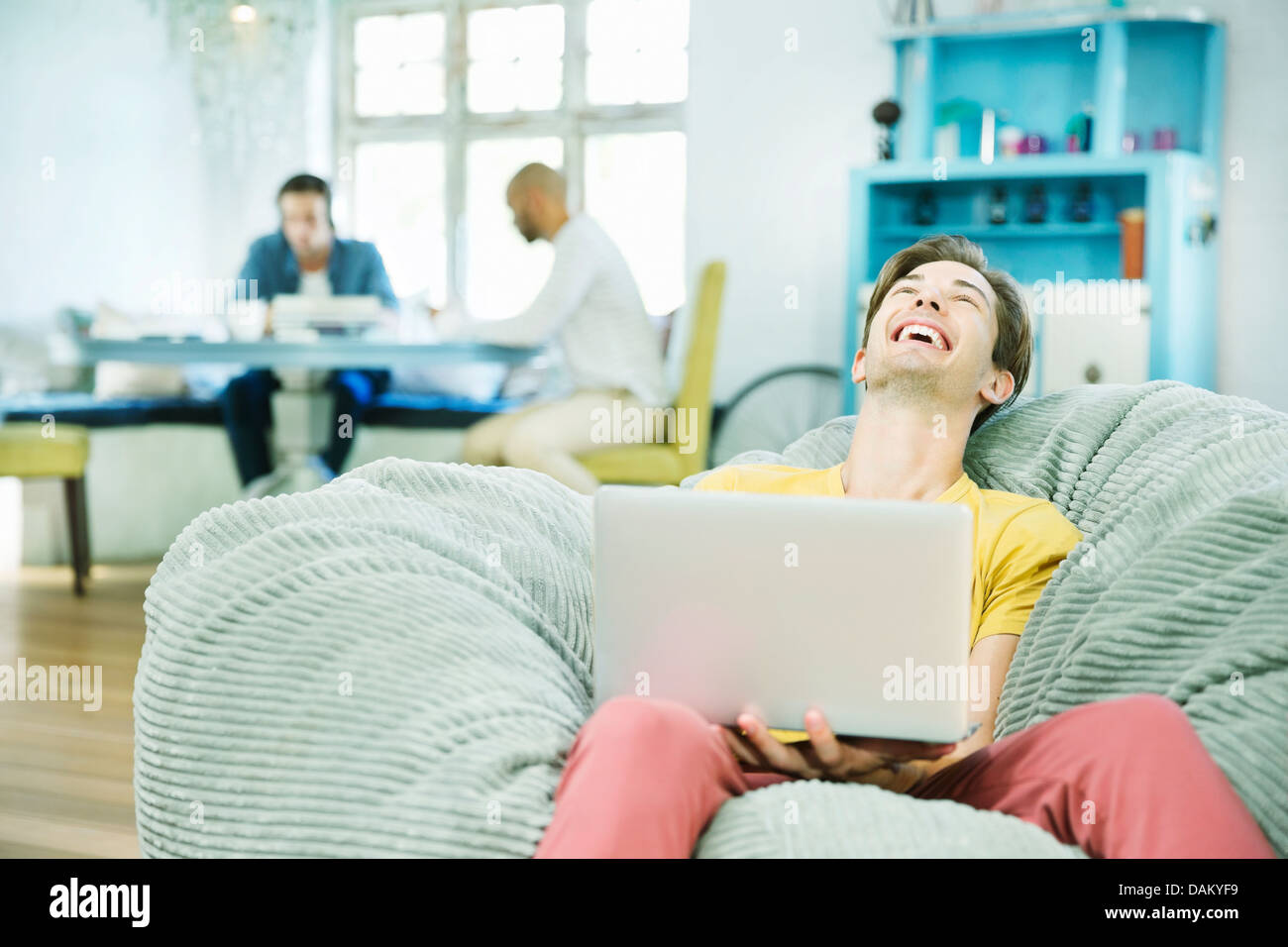 Laughing Man utilizzando laptop nella sedia beanbag Foto Stock