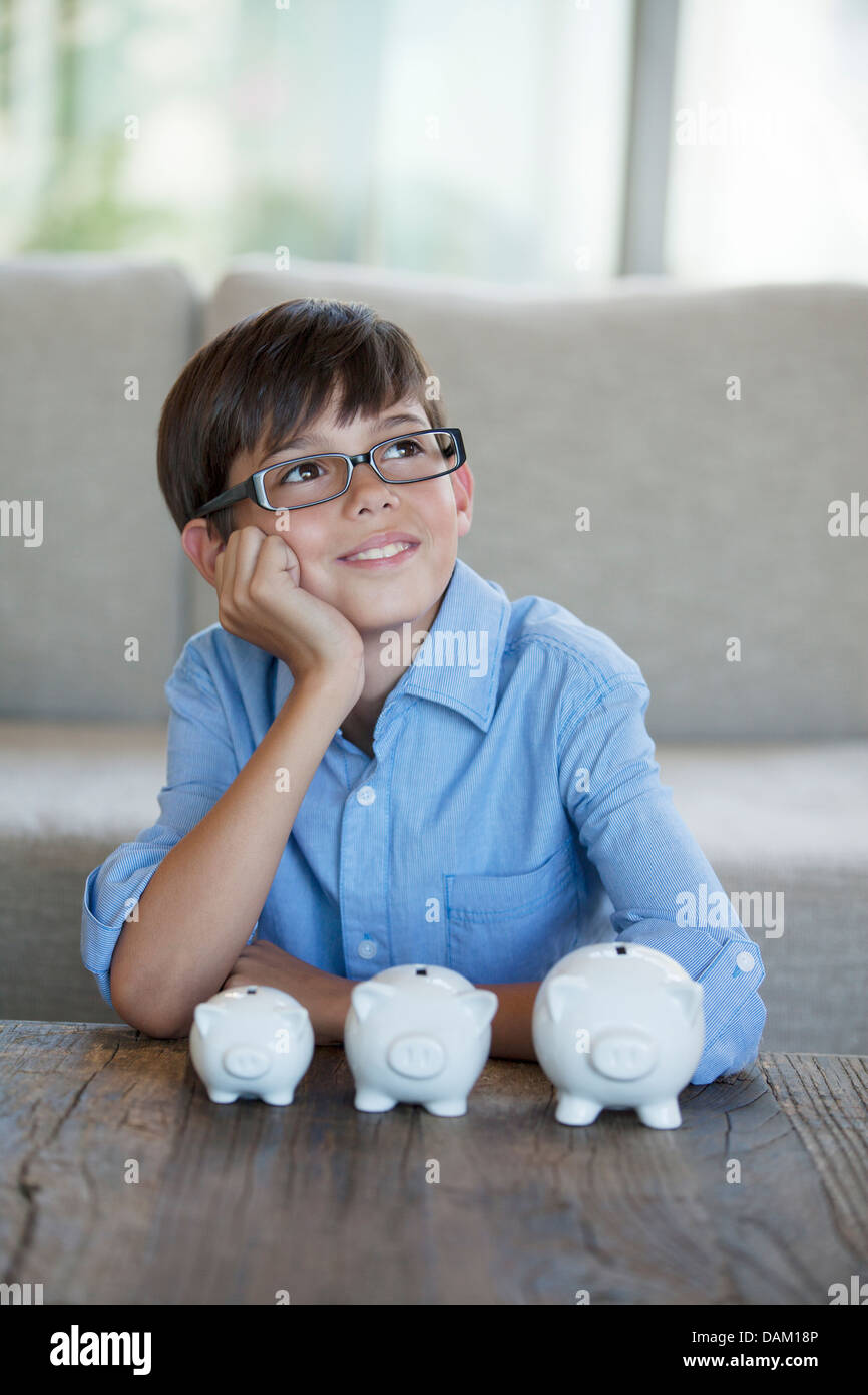 Ragazzo seduto con piggy banche a tavolino Foto Stock