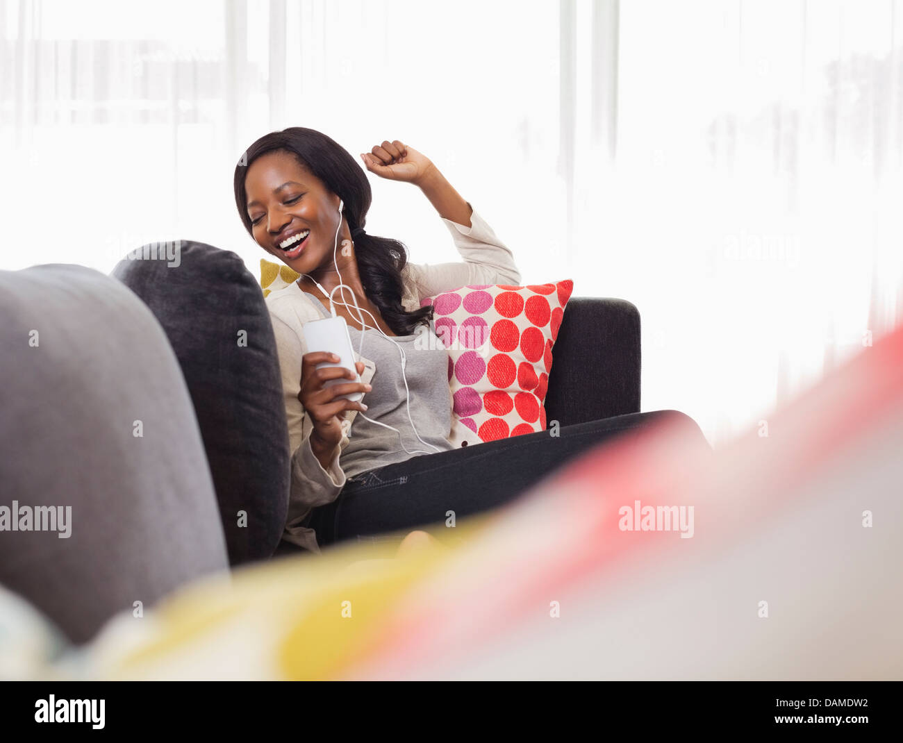 Donna in ascolto delle cuffie sul divano Foto Stock