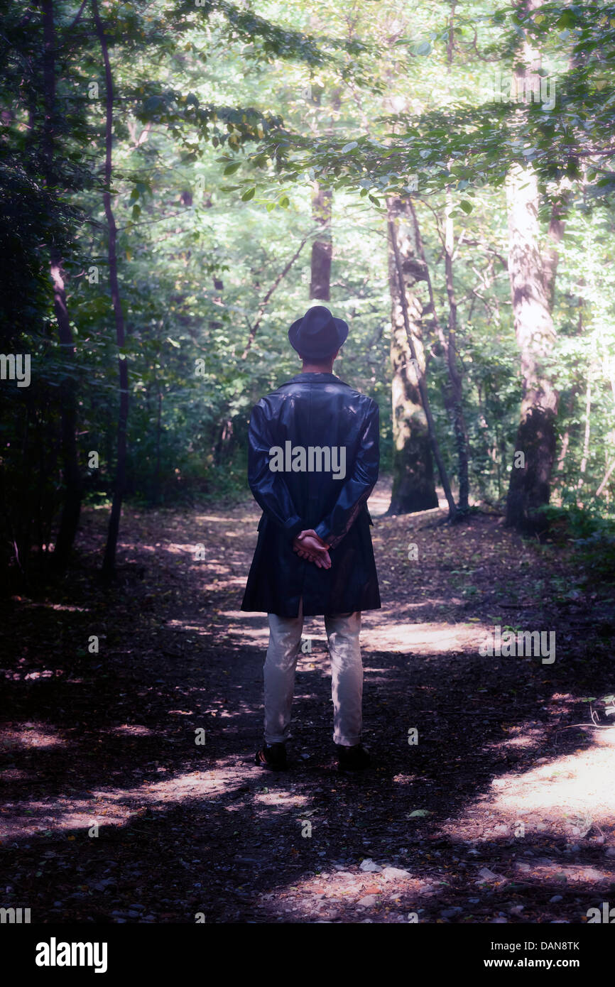 Un uomo con cappello nero e giacca di pelle è in piedi nel bosco Foto Stock