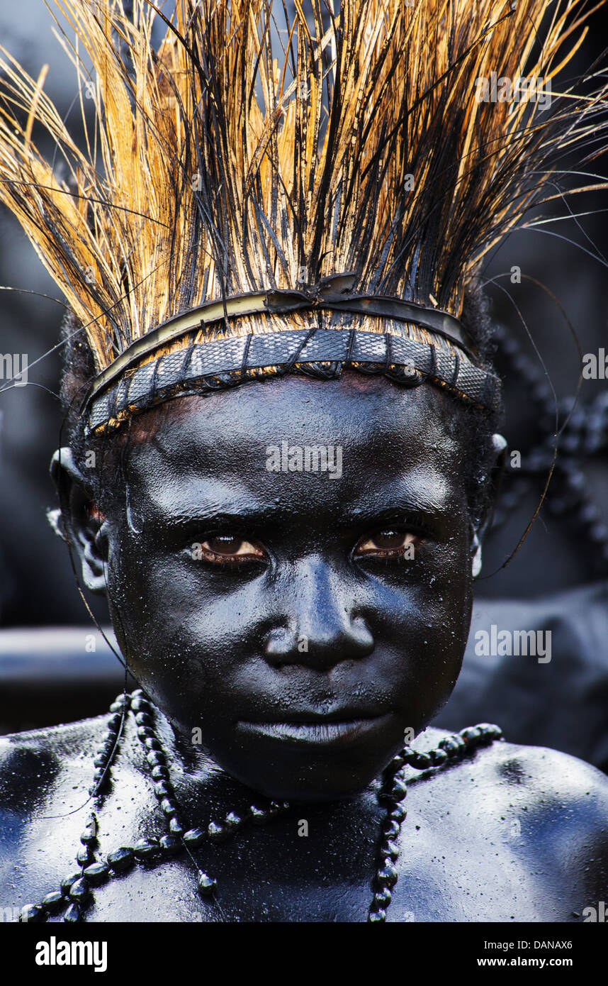 Ragazzo giovane verniciato nero lucido e indossando un copricapo di erba a Goroka show in Papua Nuova Guinea Foto Stock