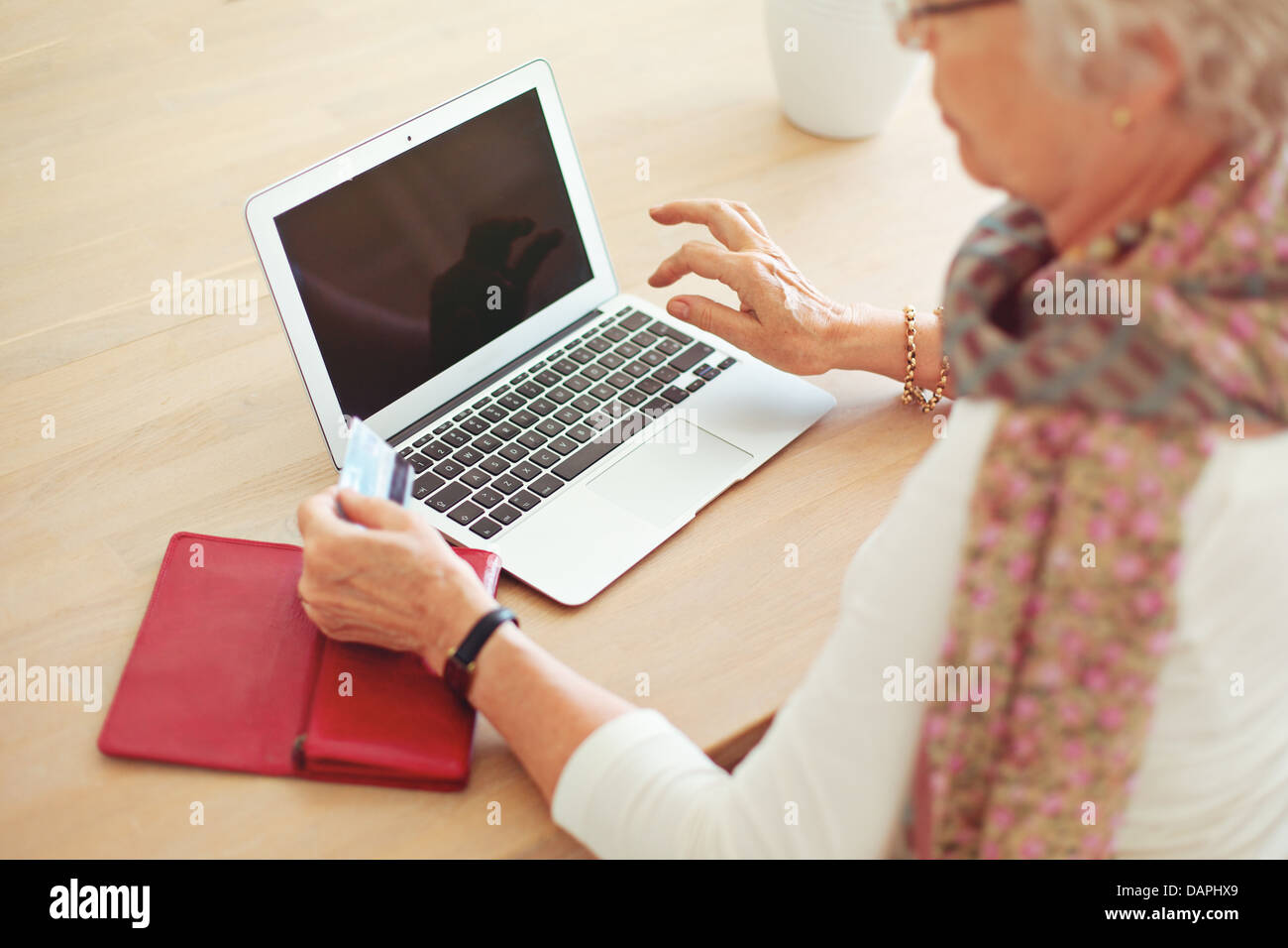 Vecchia donna in possesso di una carta di credito nella parte anteriore del computer portatile con schermo vuoto Foto Stock