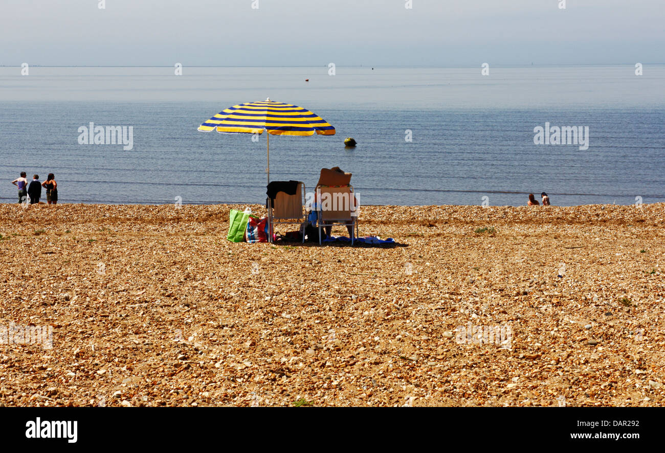 Una vista di una signora sotto un ombrello riparo dal sole sulla spiaggia a Snettisham, Norfolk, Inghilterra, Regno Unito. Foto Stock
