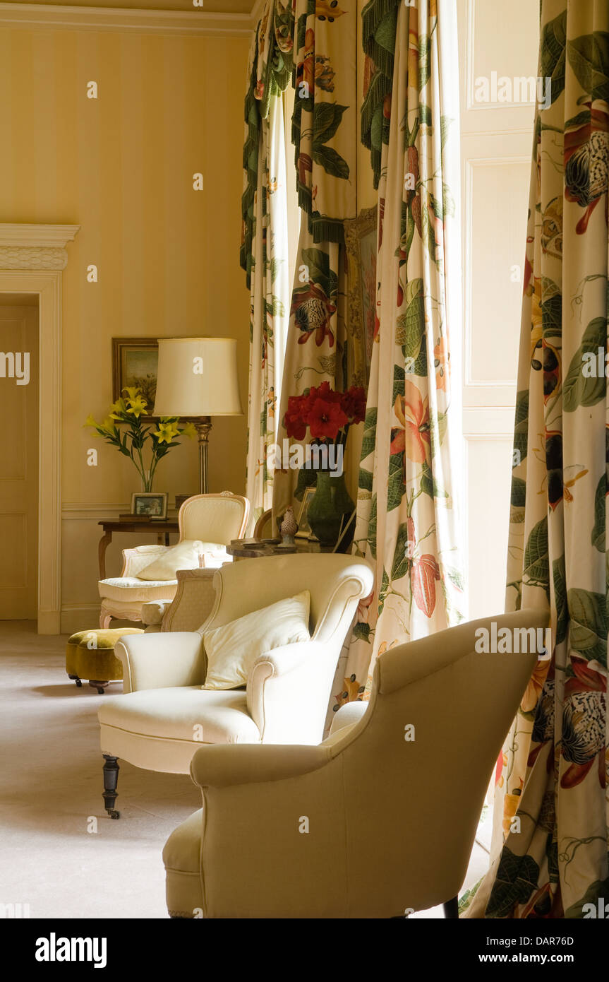 Poltrone imbottite e full-length tende floreali in giallo sala di ricevimento di English Manor House, Ampney Park Foto Stock