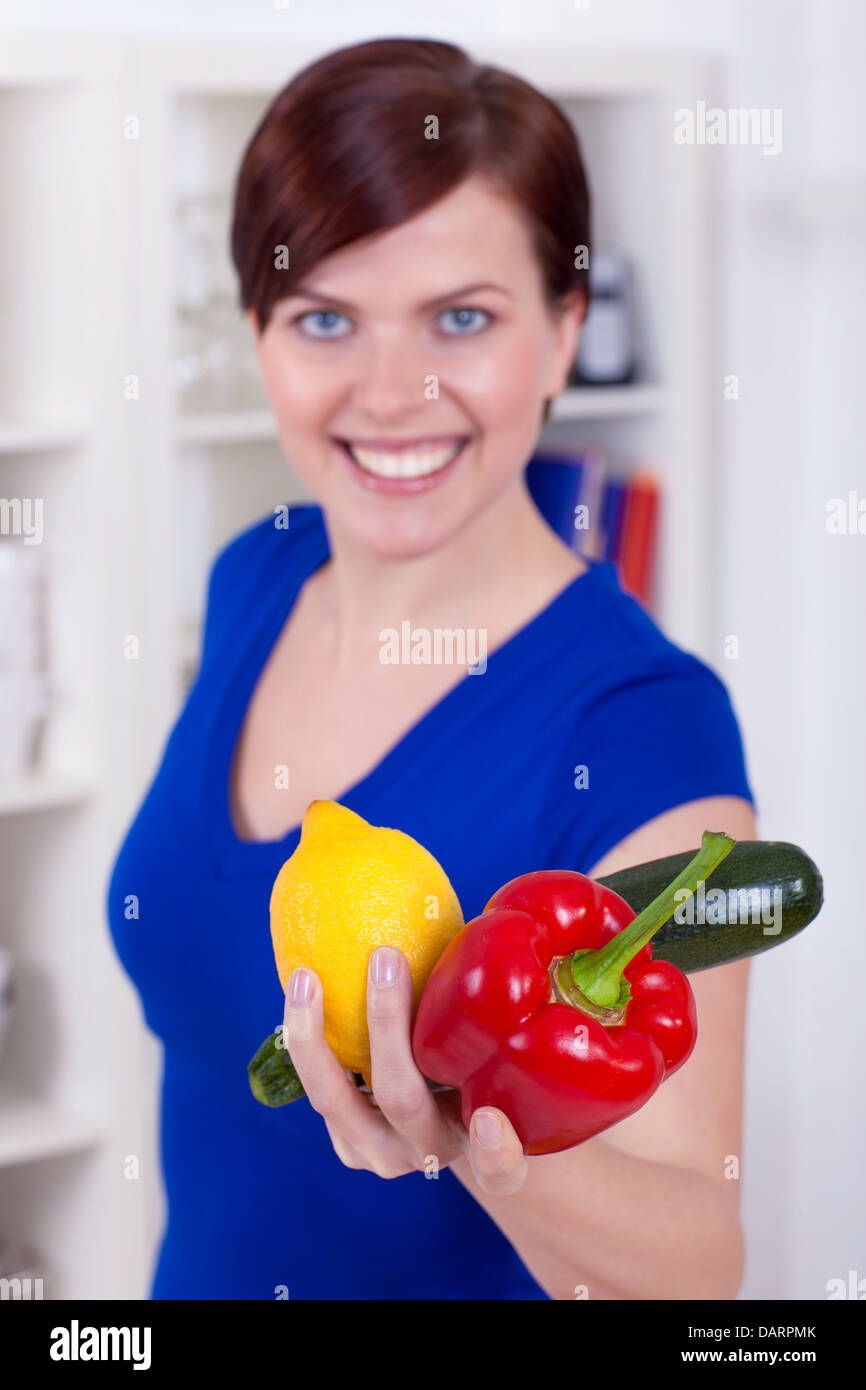 Bella giovane donna sta offrendo le verdure nella sua cucina Foto Stock