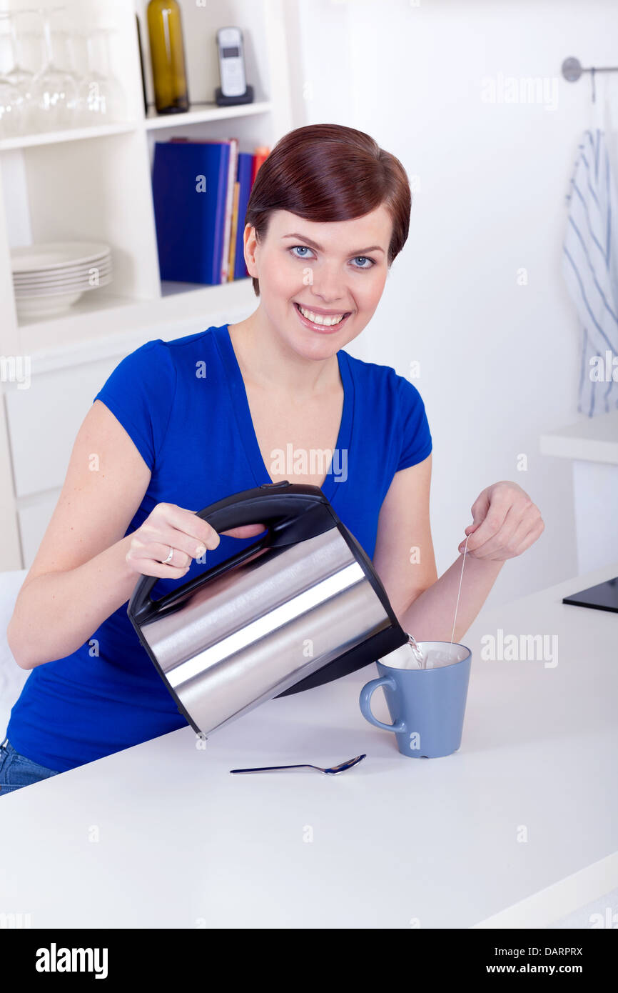 Giovane e bella felice giovane donna preparando il tè a casa al mattino Foto Stock