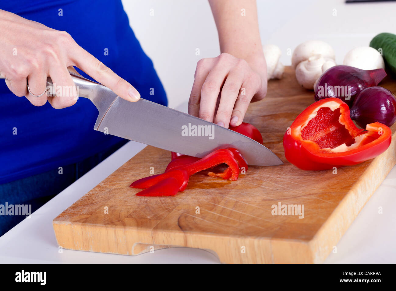 Mani femminili tritare verdure su una tavola di legno in cucina Foto Stock