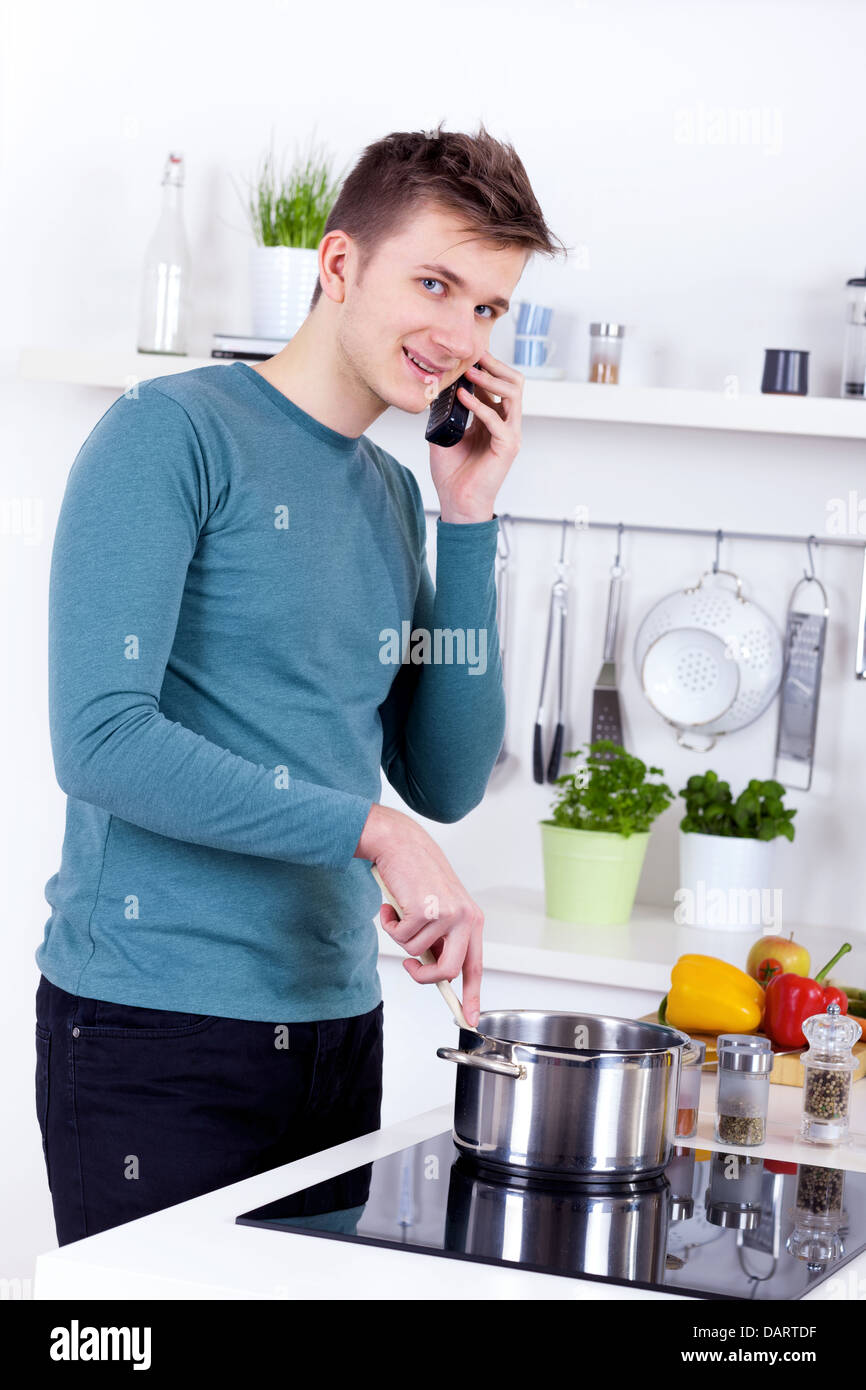 Giovane uomo cucinare un pasto e parlando al telefono nella sua cucina Foto Stock