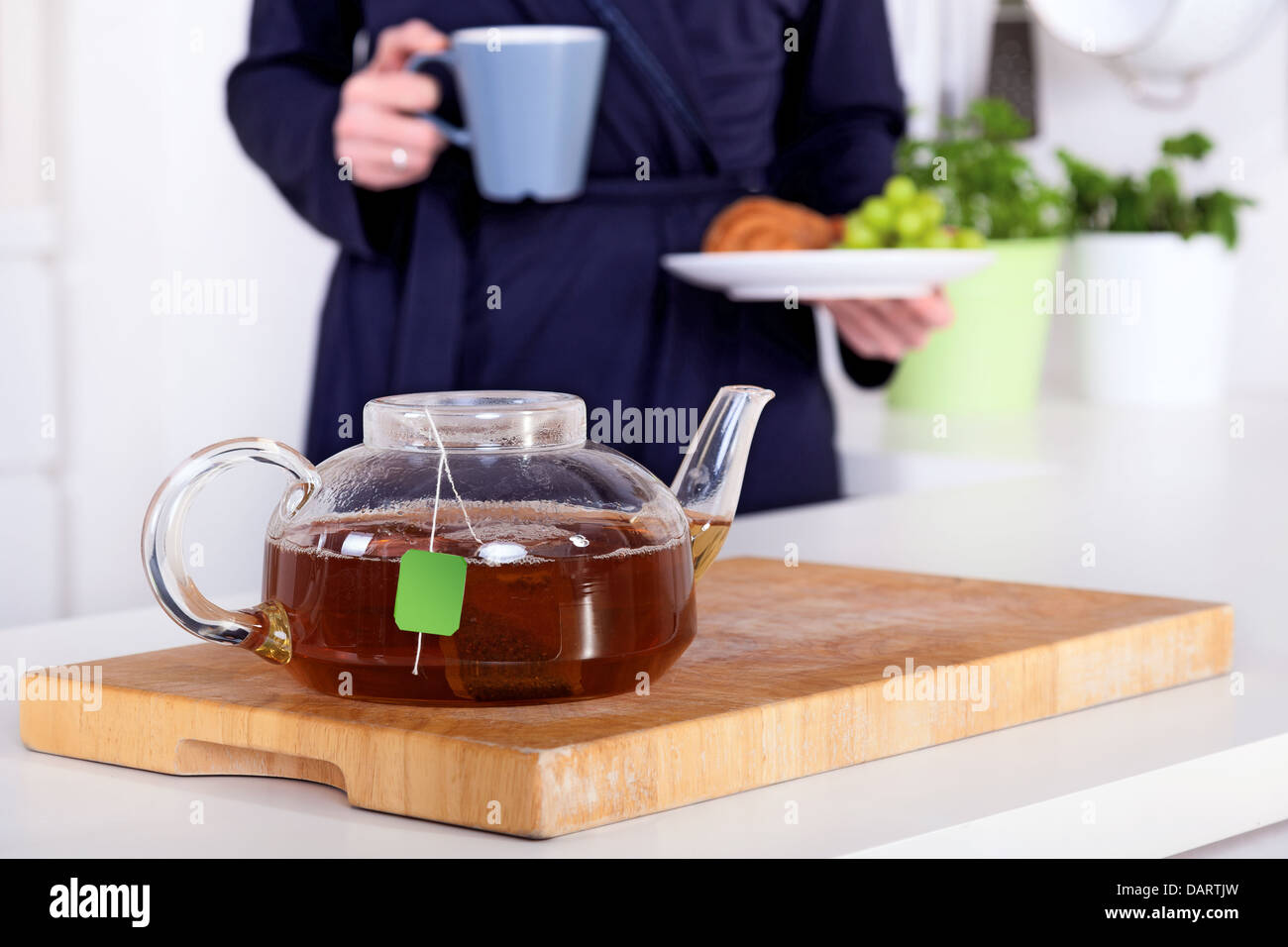 Pentola di tè e la donna in possesso di una sana colazione in background Foto Stock