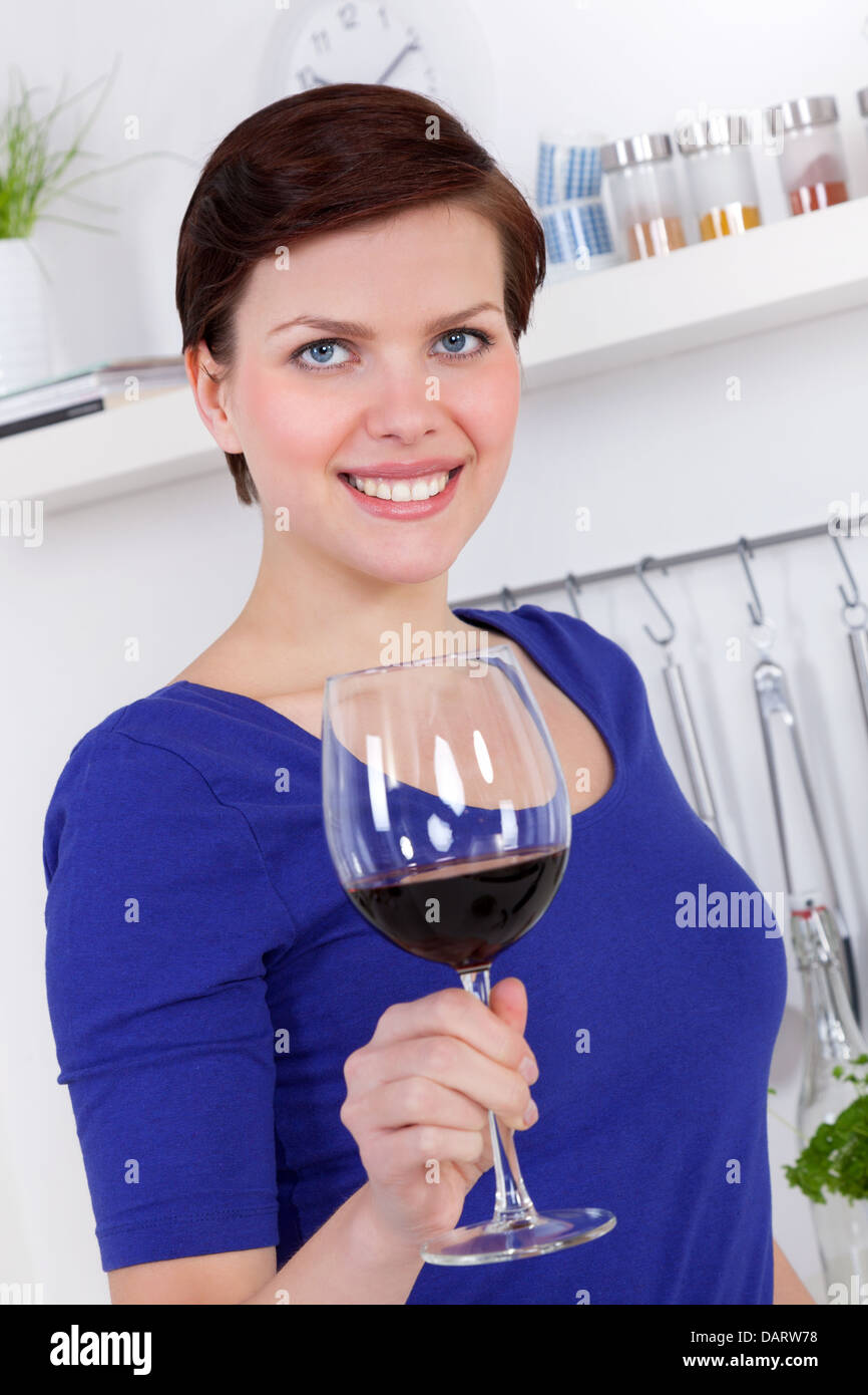 Giovane donna gustando un bicchiere di vino rosso nella sua cucina moderna Foto Stock
