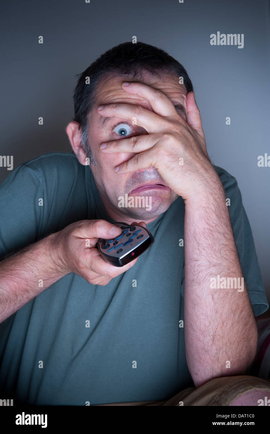 Uomo che ricopre la faccia guardare la tv o la televisione ha paura o spaventato Foto Stock