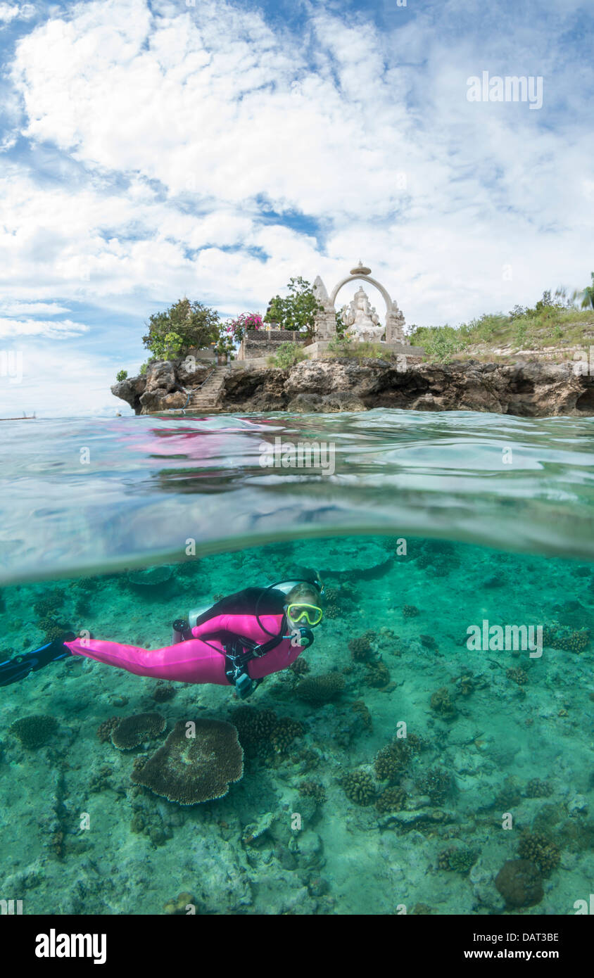 A livello diviso Vista del biondo sub femmina esplorazione subacquea al fianco di isola tropicale con un tempio indù in background Foto Stock