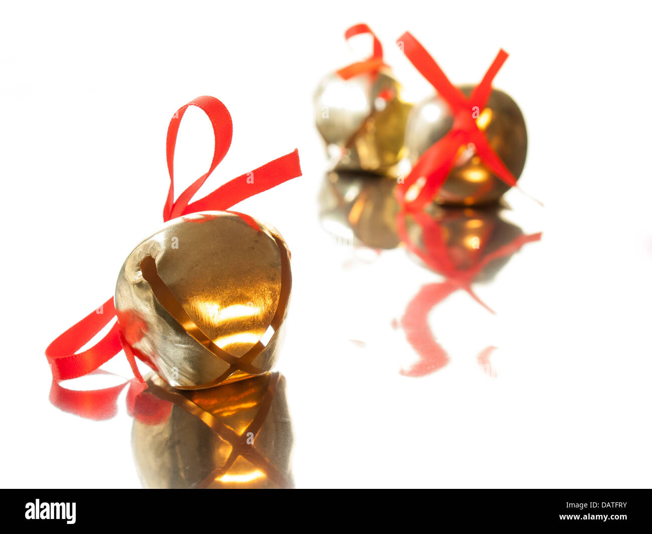 Shiny golden sleigh campana con nastro rosso arco sulla superficie riflettente con sleigh bells fuori fuoco in background Foto Stock