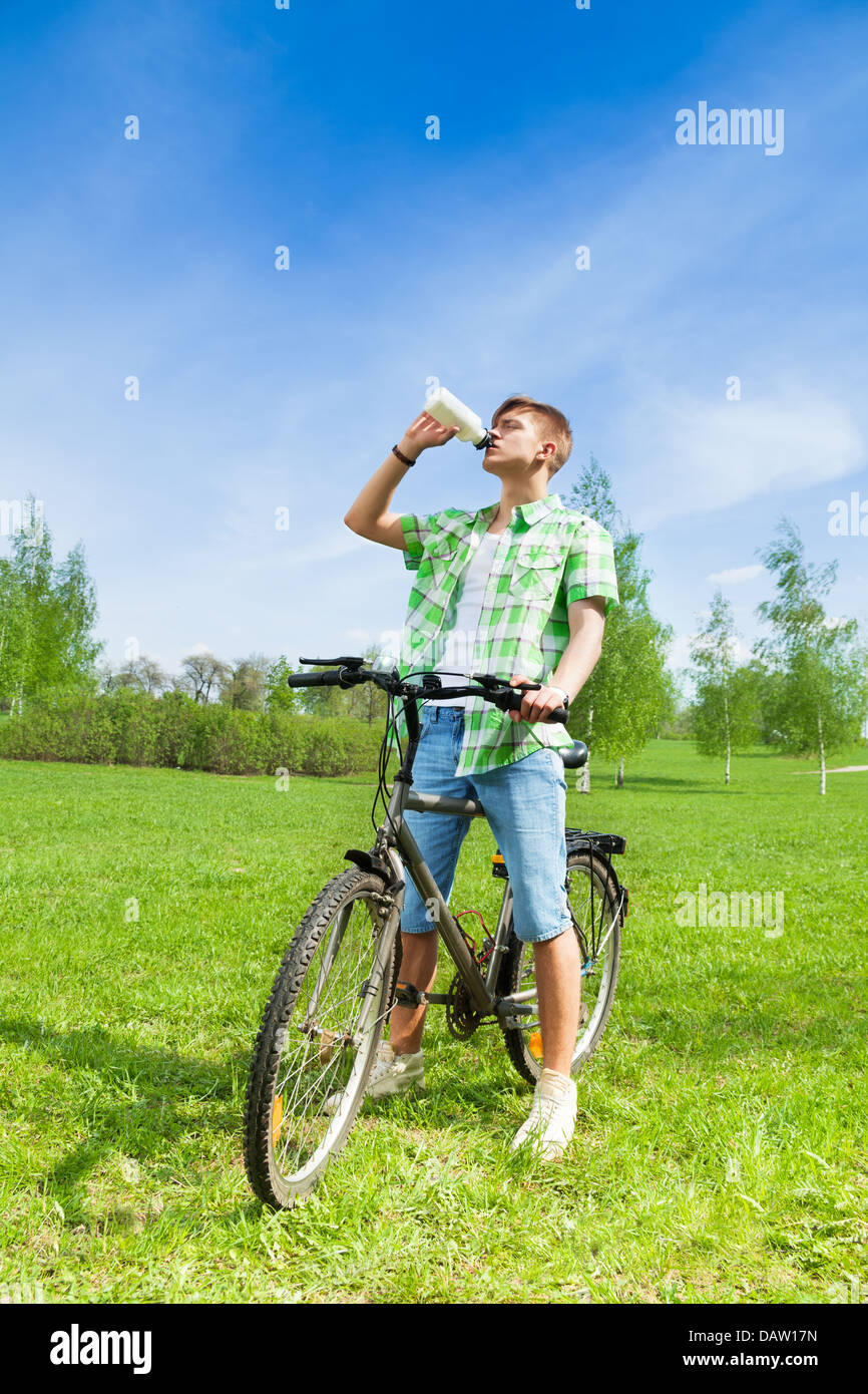 Giovane uomo seduto su una bicicletta e di acqua potabile in una bottiglia in un parco Foto Stock