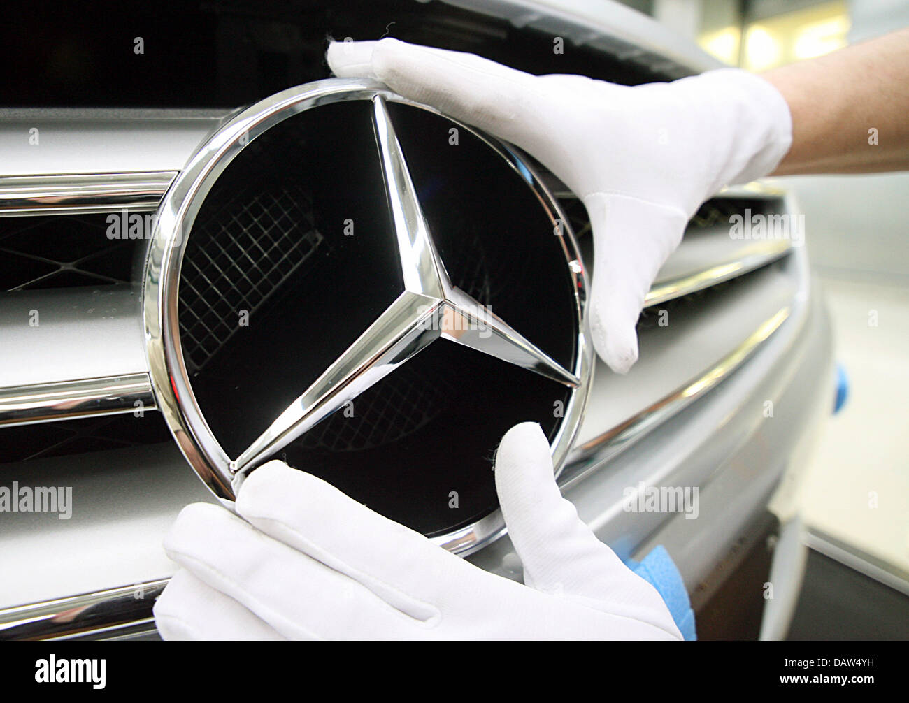 Un dipendente di costruttore DaimlerChrysler AG indossando i guanti di cotone bianco fissa la famosa stella a tre punte con un anello normale Mercedes Benz logo sulla griglia del radiatore di una Mercedes Benz Classe S berlina presso lo stabilimento della società in Sindelfingen, Germania, Venerdì, 02 febbraio 2007. DaimlerChrysler impiega 29,900 persone a livello mondiale la sua più grande impianto di produzione in Sindelfingen, che da Foto Stock