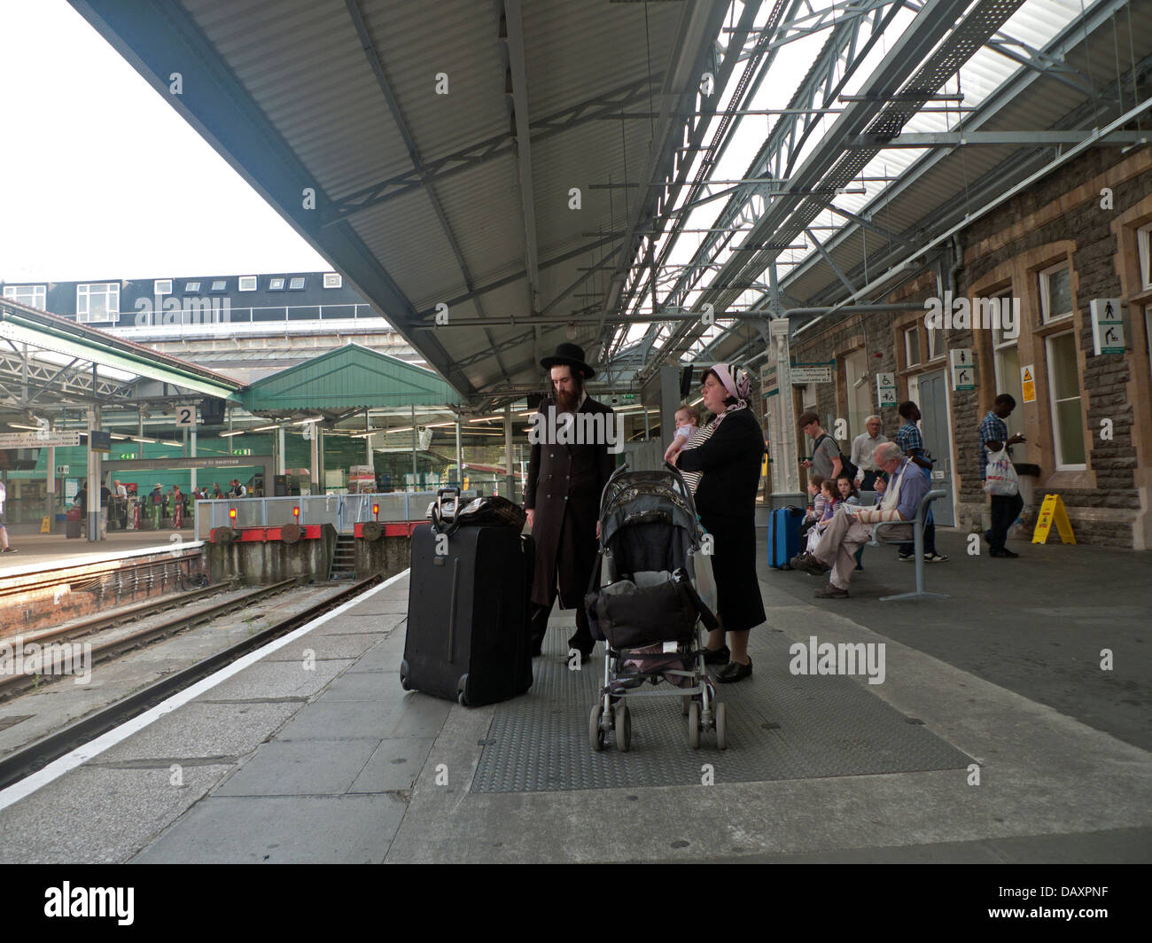 Un Hasidic famiglia ebraica in attesa di un treno in stazione Ferroviaria Swansea piattaforma con bagagli e baby buggy in estate Wales UK Foto Stock
