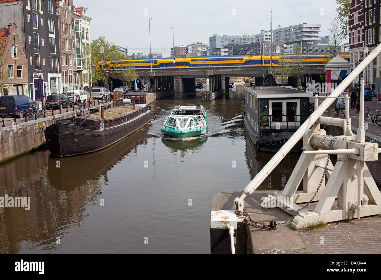 Paesaggio urbano di Amsterdam nei Paesi Bassi, canal con case galleggianti e nave passeggeri, condomini, treno su un ponte. Foto Stock