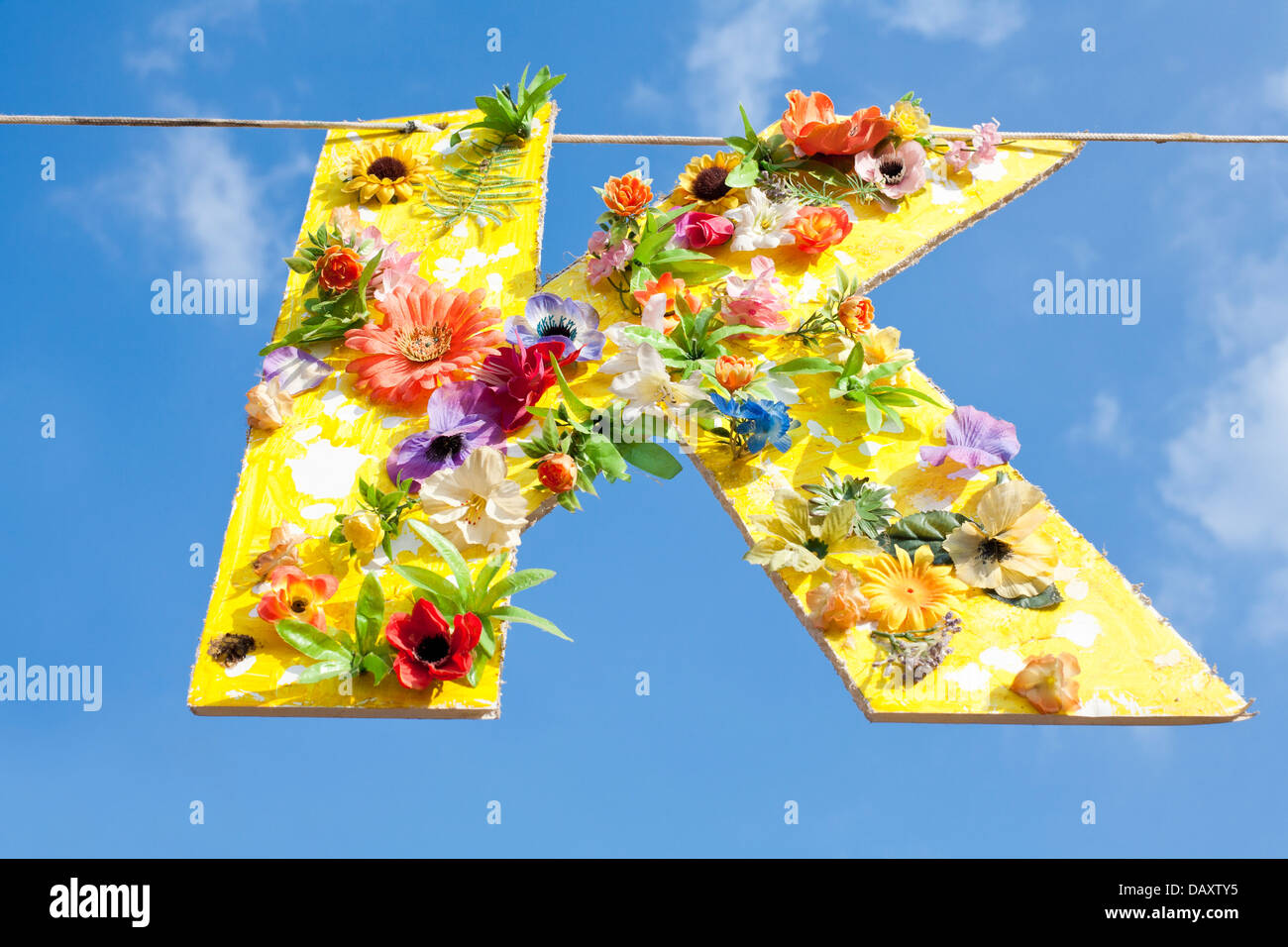 Ritaglio di cartone della lettera K, dipinte di giallo e coperto di fiori. Appesi su una linea contro un Cielo di estate blu. Foto Stock