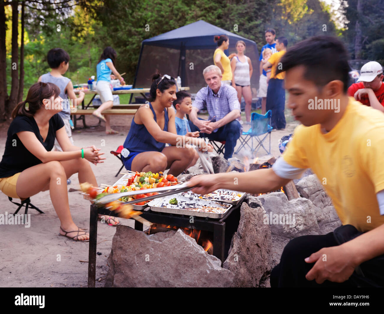 Un gruppo di persone di diverse etnie che si diverte seduti attorno a un fuoco in un campeggio in un parco. In Ontario, Canada. Foto Stock