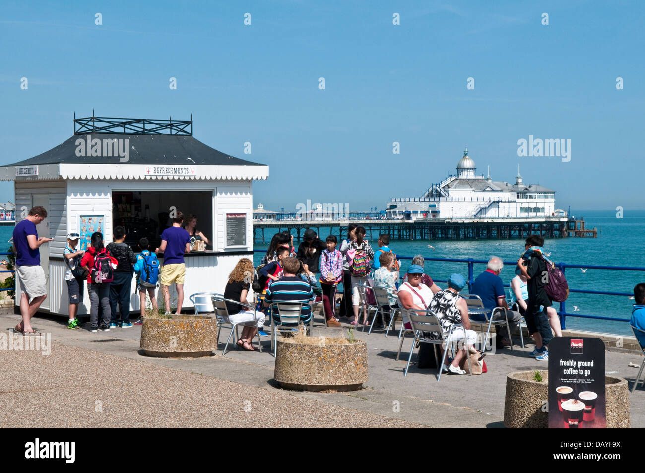 I turisti in un chiosco ristoro sul lungomare di Eastbourne con il molo in background Foto Stock