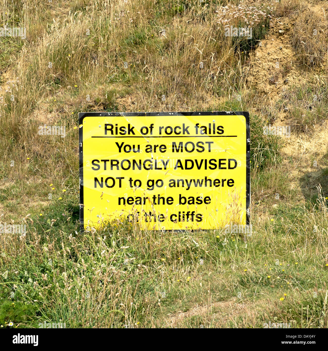 Cartello giallo con scritte nere di avvertimento del pericolo di frane impostato su pascoli a Freshwater Bay Dorset Regno Unito Foto Stock