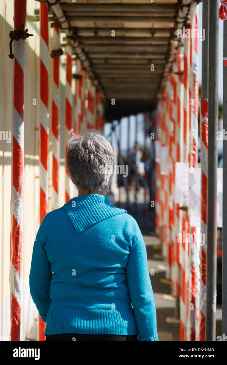 La donna a piedi attraverso un ponteggio sulla proprietà per la riparazione Foto Stock