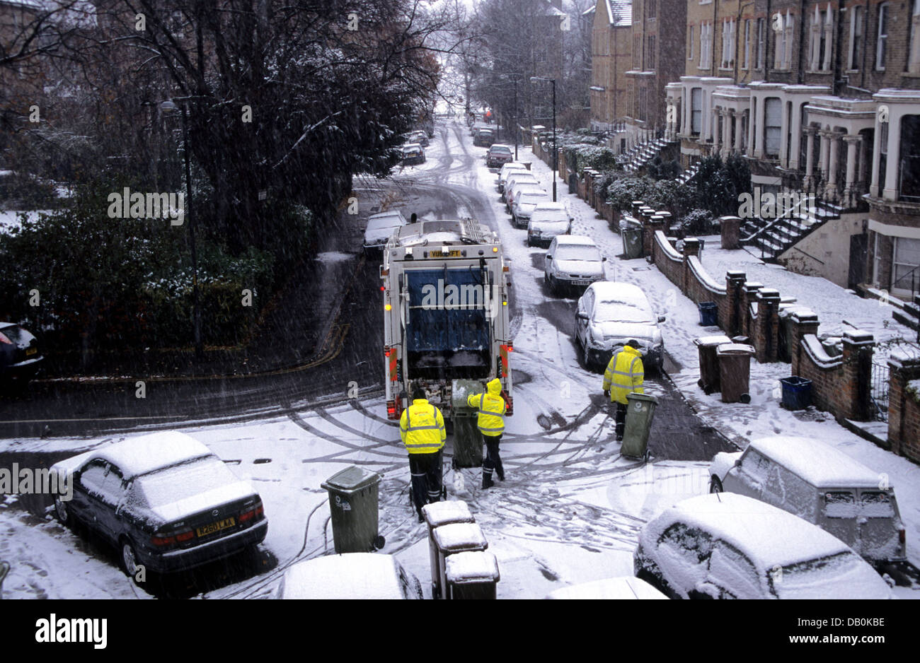 Raccolta rifiuti con bidoni in una strada suburbana nevosa di Londra in inverno, Inghilterra Foto Stock