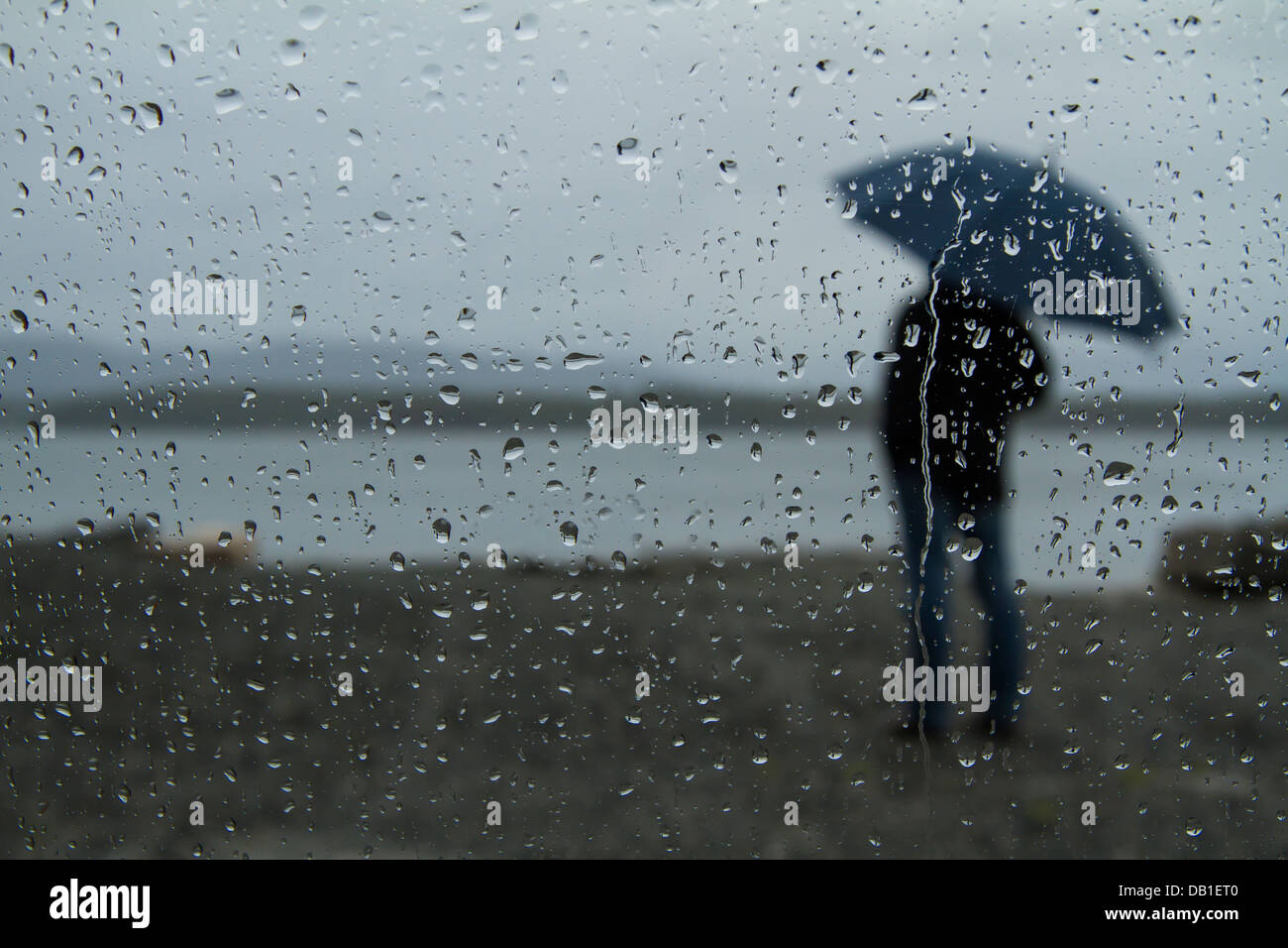 Guardando attraverso la finestra con le gocce di pioggia vedendo un uomo  solo in piedi sotto la pioggia con ombrello blu Foto stock - Alamy