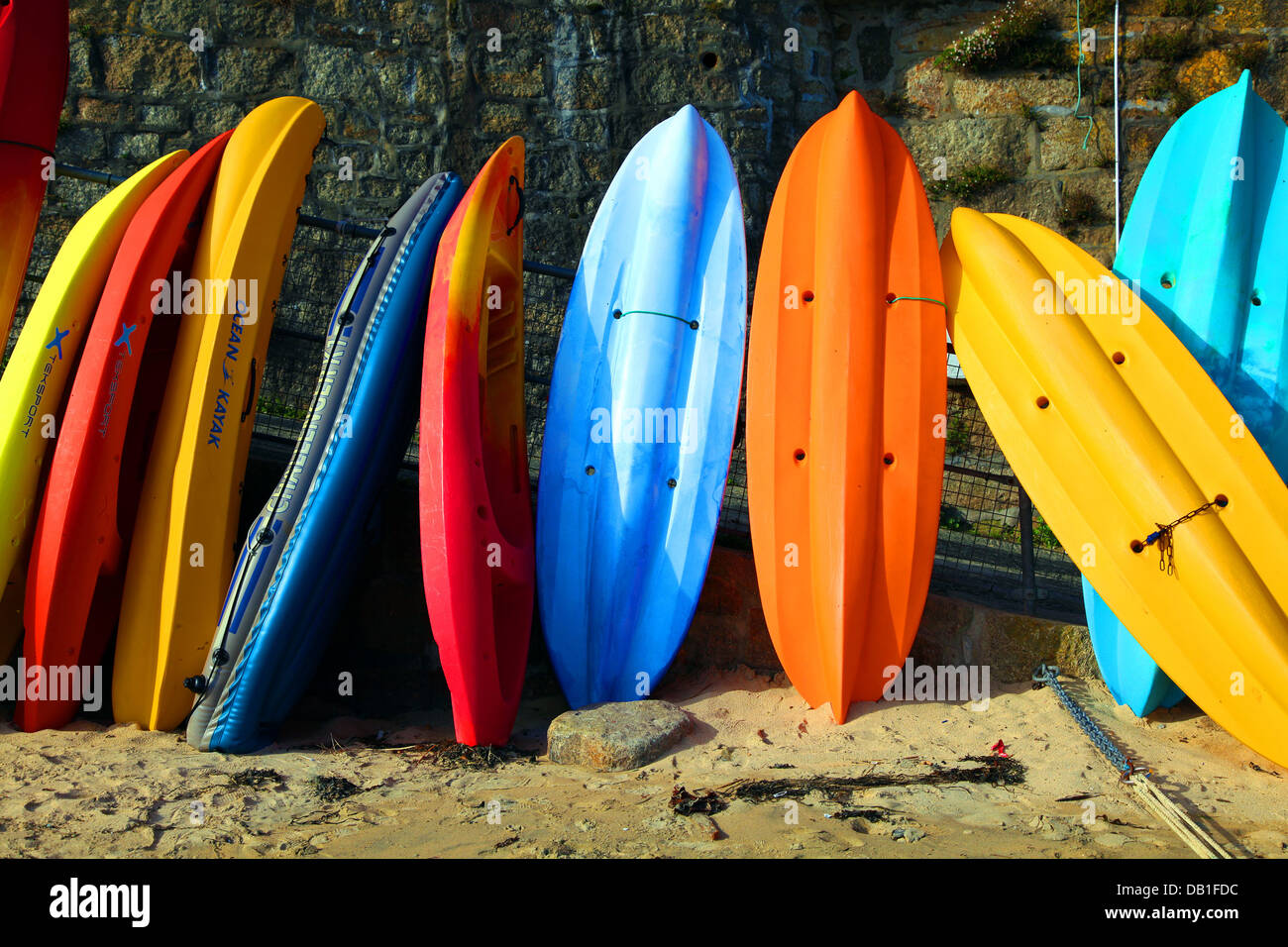 Una fila di vivacemente colorato kayak sit contro una parete del porto in Cornovaglia. Foto Stock