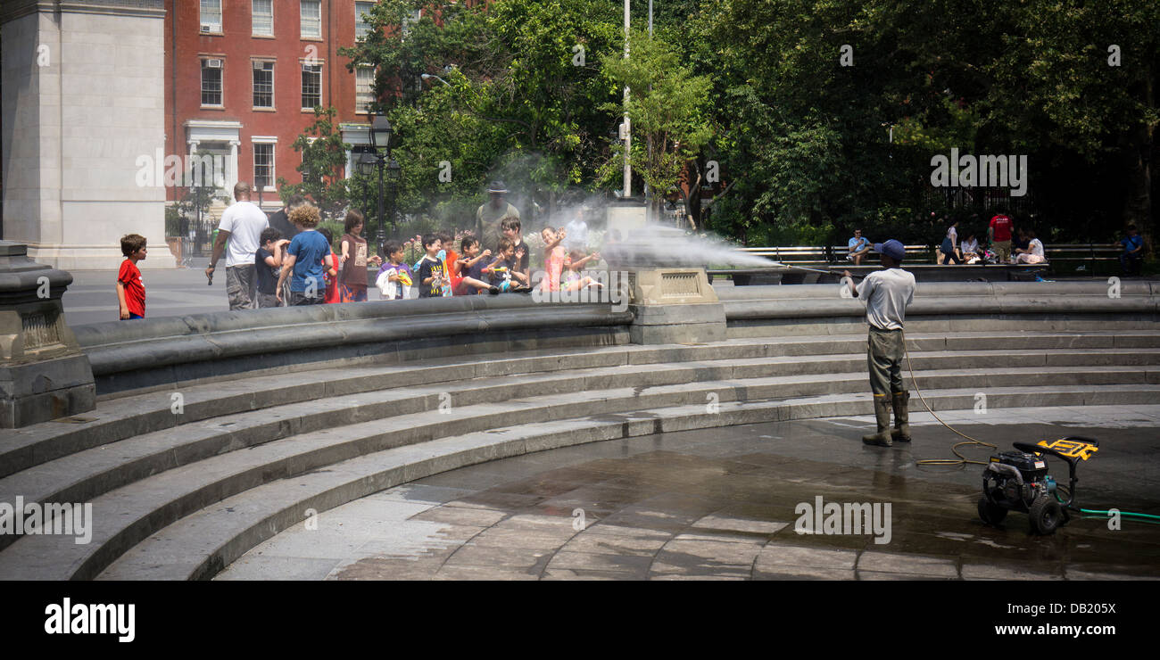 Un NYC Dept. di parchi lavoratore spruzza acqua calda passante su richiesta come lui pulisce la fontana di Washington Square Park Foto Stock