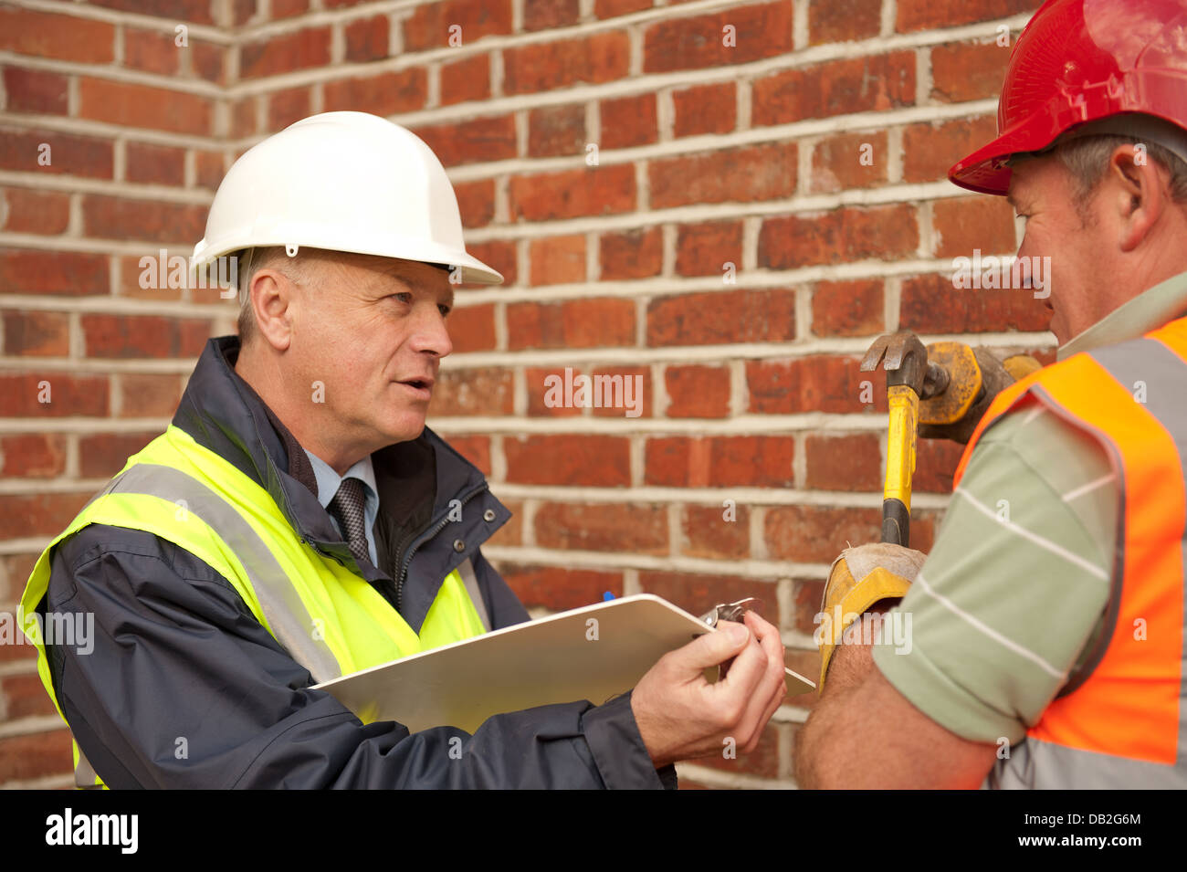 Due lavoratori edili in corso circa i loro doveri. Responsabile del sito con un operaio generale, entrambi a parlare e discutere il lavoro. Foto Stock