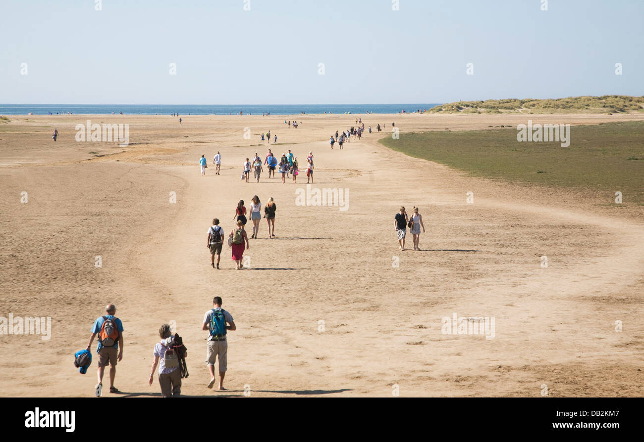 Persone che camminano verso il mare attraverso ampia spiaggia sabbiosa Holkham Norfolk Inghilterra Foto Stock