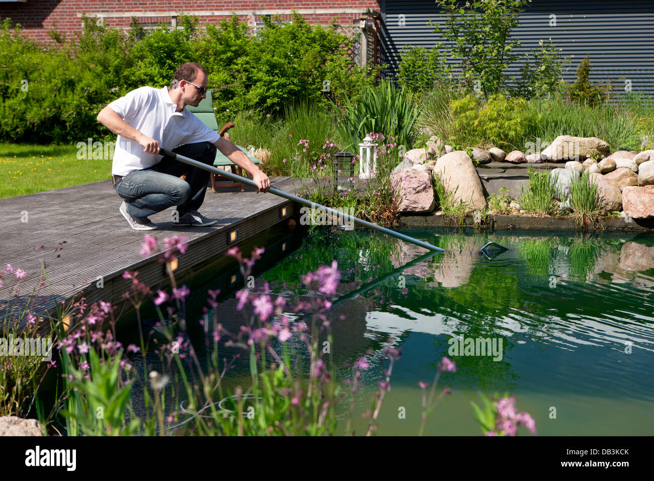 L'uomo inginocchiati su una terrazza in legno e pesca con una rete in stagno Foto Stock