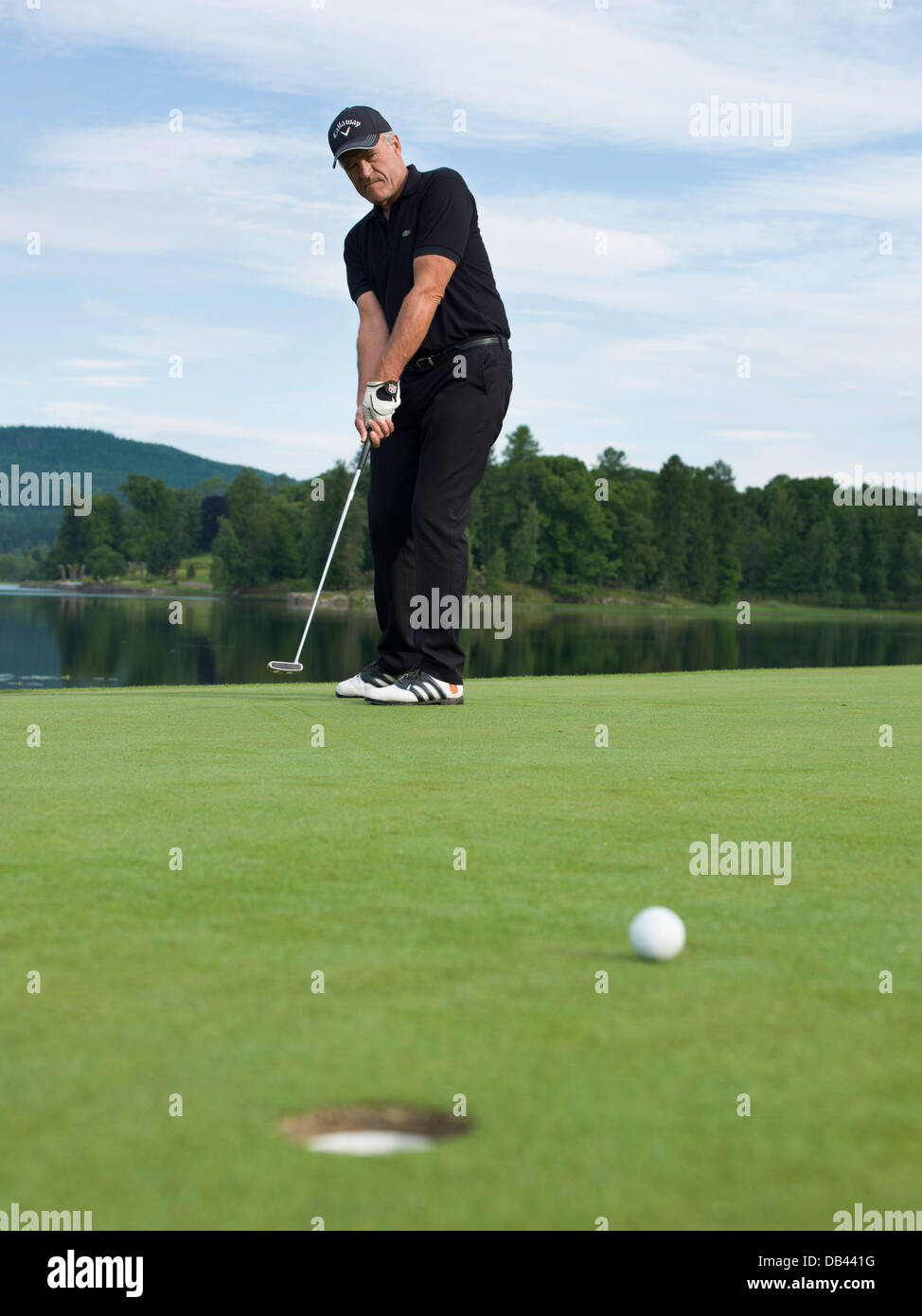 Senior Citizen giocando a golf, vestito di nero. Azione girato sul verde Foto Stock