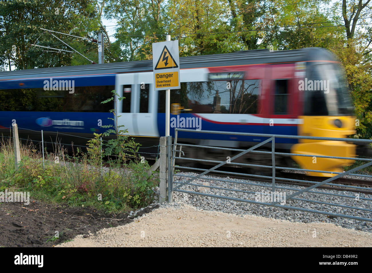 Locale treno passeggeri motore acceso sulla linea Wharfedale, velocità & viaggi passato gate & sicurezza segno di avvertimento - Esholt, West Yorkshire, Inghilterra, Regno Unito. Foto Stock