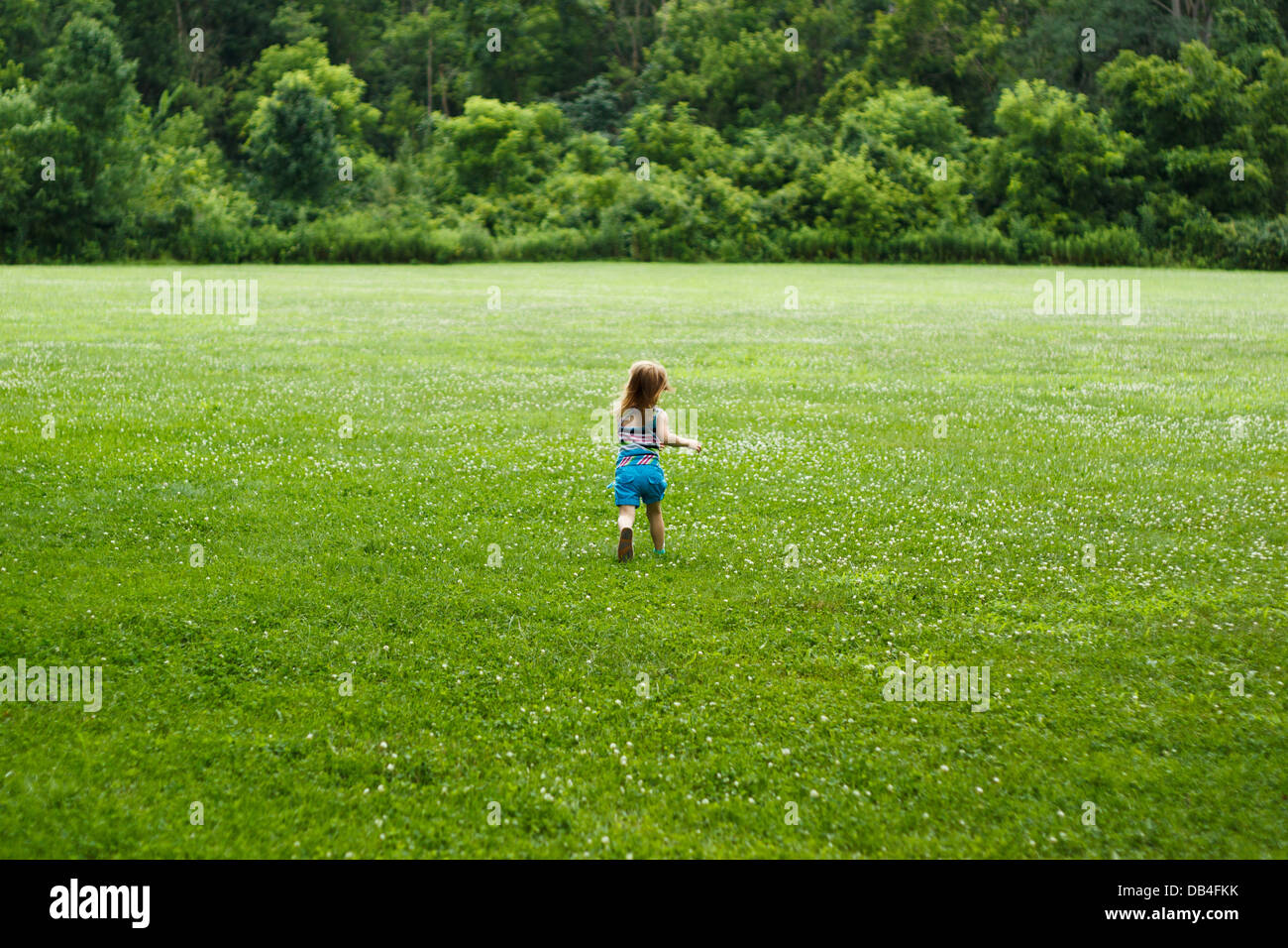 Un bambino piccolo che corre attraverso il campo verso boschi Foto Stock