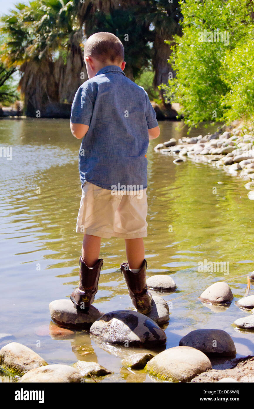 Un bambino di cinque anni, ragazzo con autismo saldi sui due scogli mentre guardando all'acqua. Foto Stock