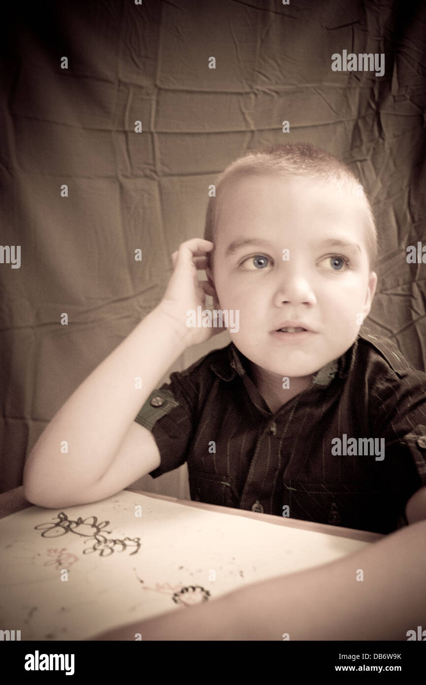 Un bambino di sei anni ragazzo con austim guarda lontano dopo il disegno di una foto, forse il pensiero del suo prossimo idea? Foto Stock