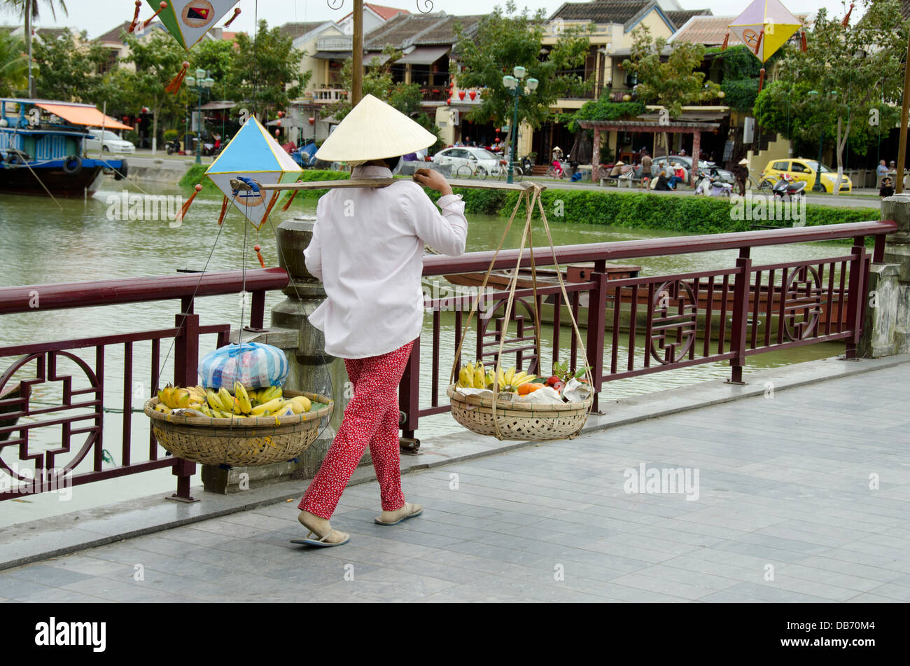 Il Vietnam, Da Nang. Hoi An. Un Hoi passerella sul fiume Thu Bon. Tipica donna nel cappello conico il trasporto di frutta. Foto Stock