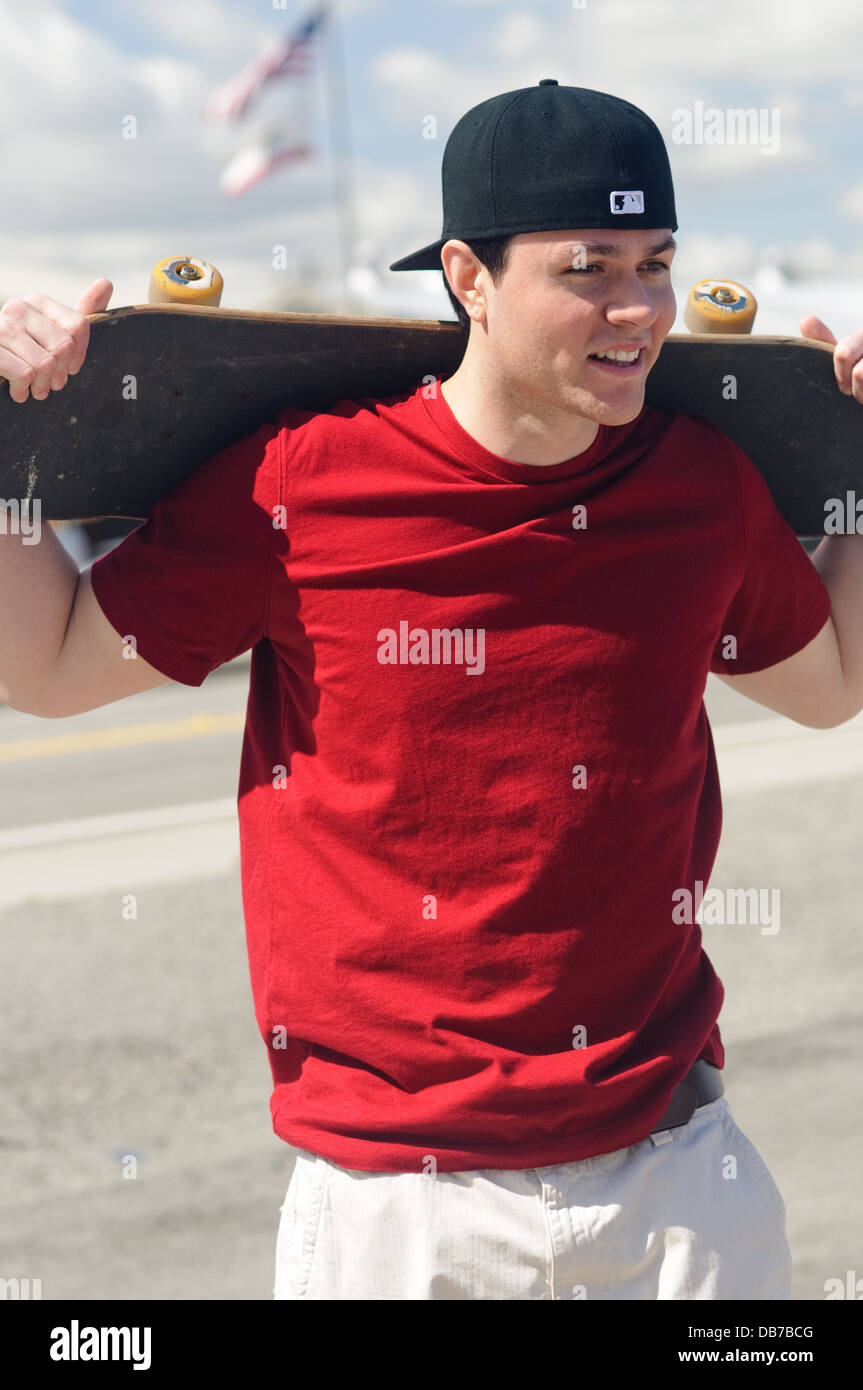 Multirazziale giovane azienda skateboard sulla spalla sorridente ritratto outdoor cielo blu sullo sfondo Foto Stock