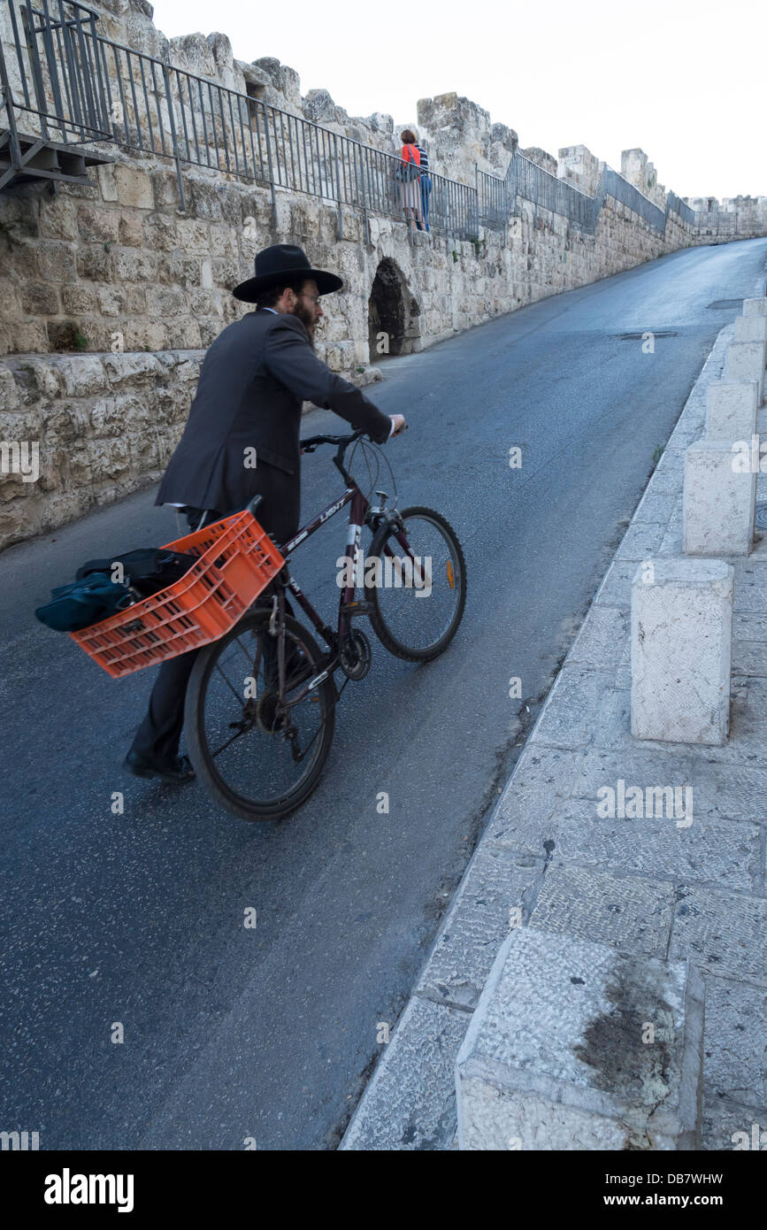 Ebreo ortodosso spingendo la sua bicicletta fino a una strada lungo le mura della città. Gerusalemme la città vecchia. Israele. Foto Stock