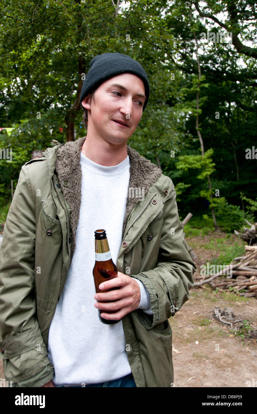 East Sussex. Giovane uomo che indossa un beanie hat e parka in possesso di una bottiglia di birra, in un bosco. Foto Stock