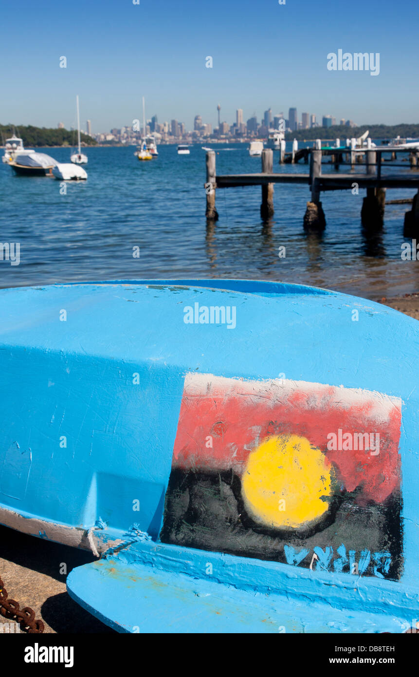 Watsons barca sulla spiaggia con bandiera aborigena dipinta sul lato dello skyline della città in distanza Sydney New South Wales (NSW) Australia Foto Stock