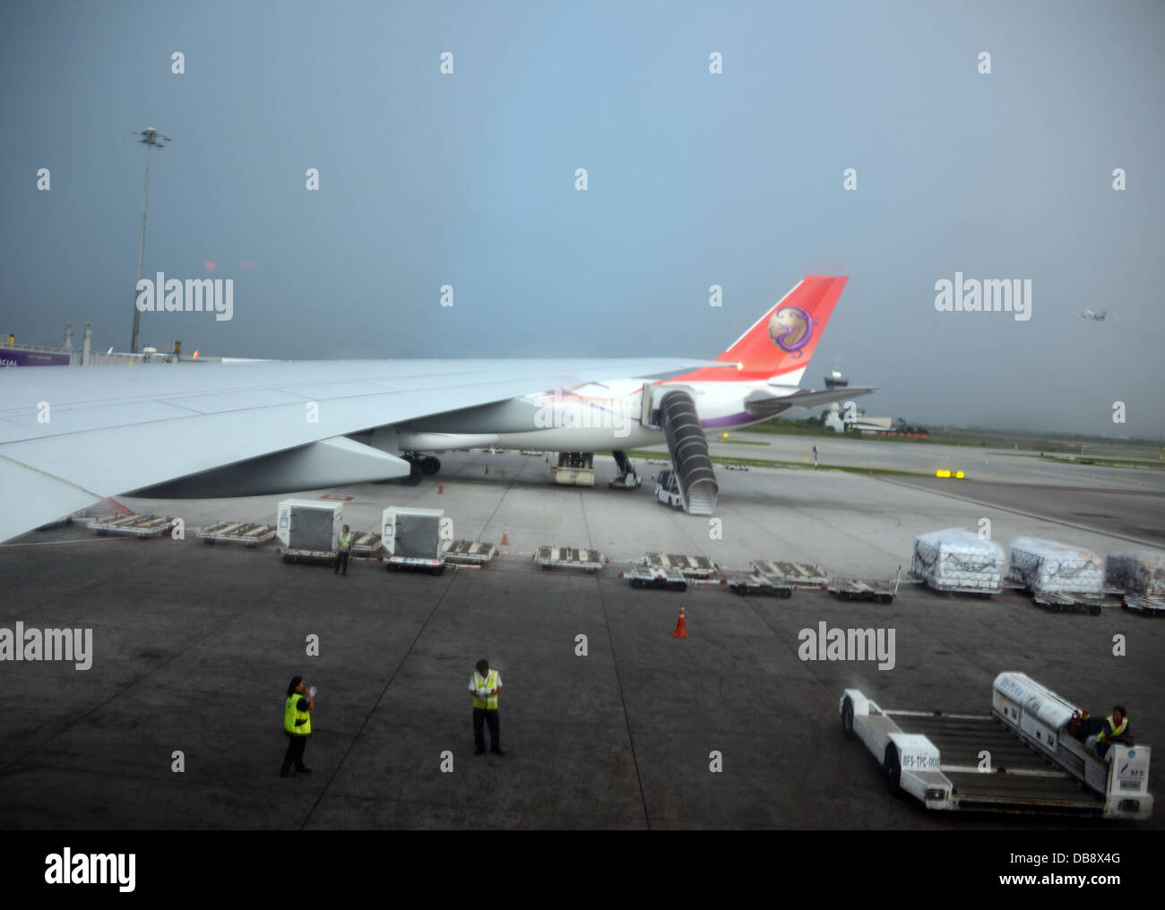 In aereo su asfalto in aeroporto con ala del piano della Tailandia e due per la sicurezza personale di rivestimento con un servizio di trasporto bagagli e carrello Foto Stock