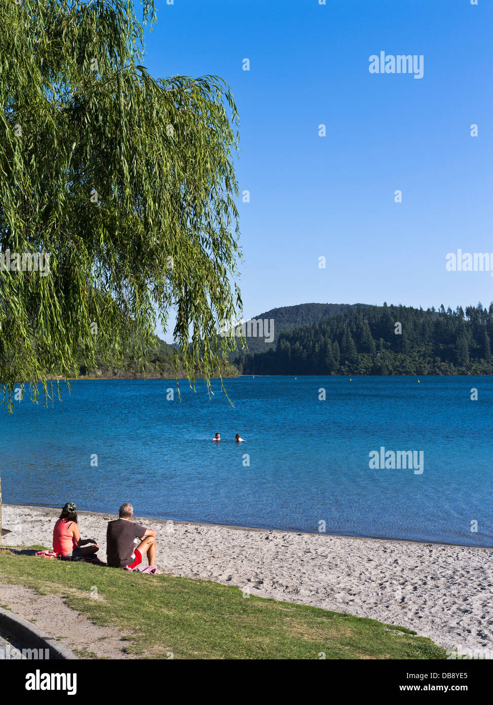 Dh Lago Blu Tikitapu Rotorua Nuova Zelanda giovane seduta rilassante sulla riva nuotatori holiday persone Foto Stock